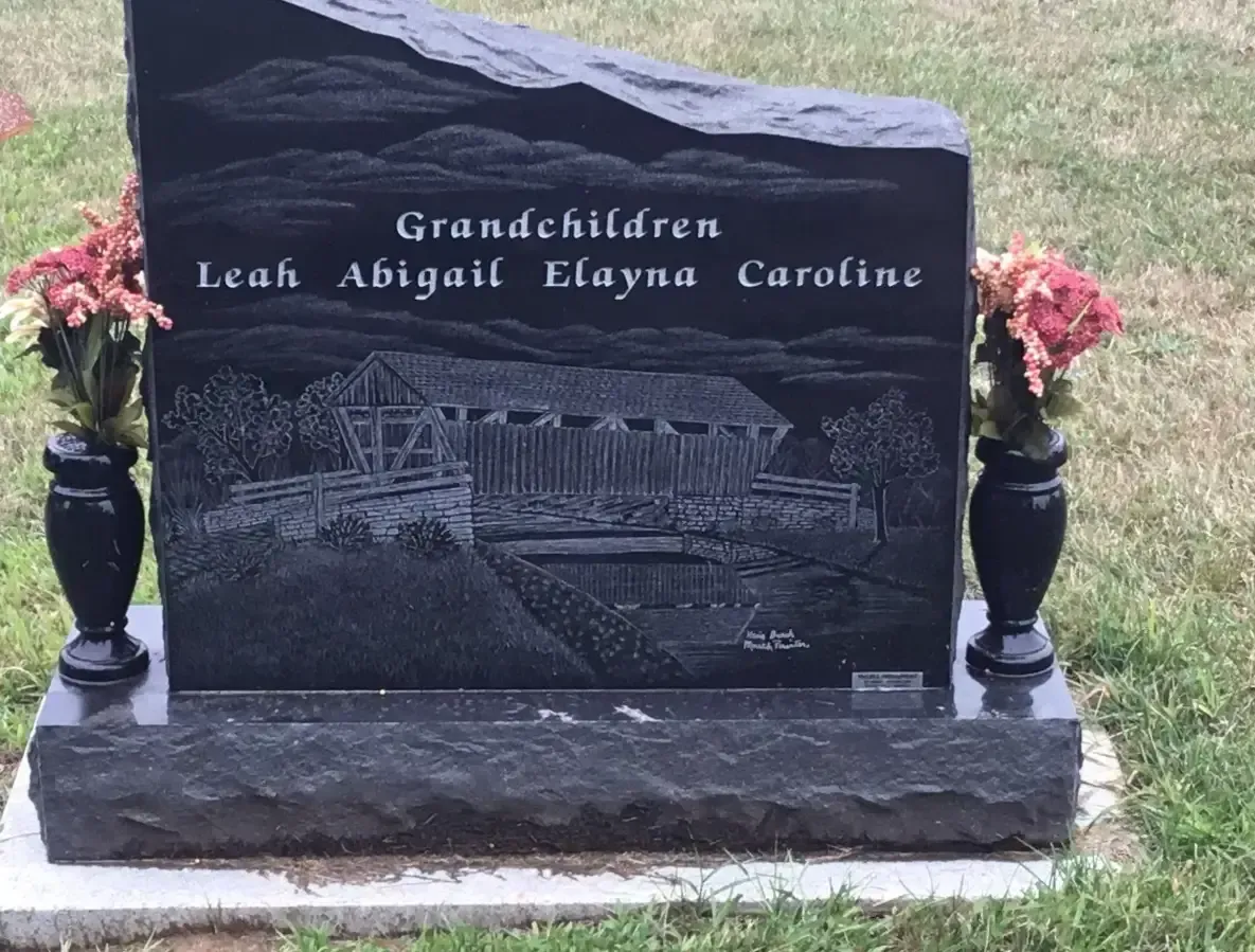 Black memorial stone with engraved text and flowers in a grassy cemetery