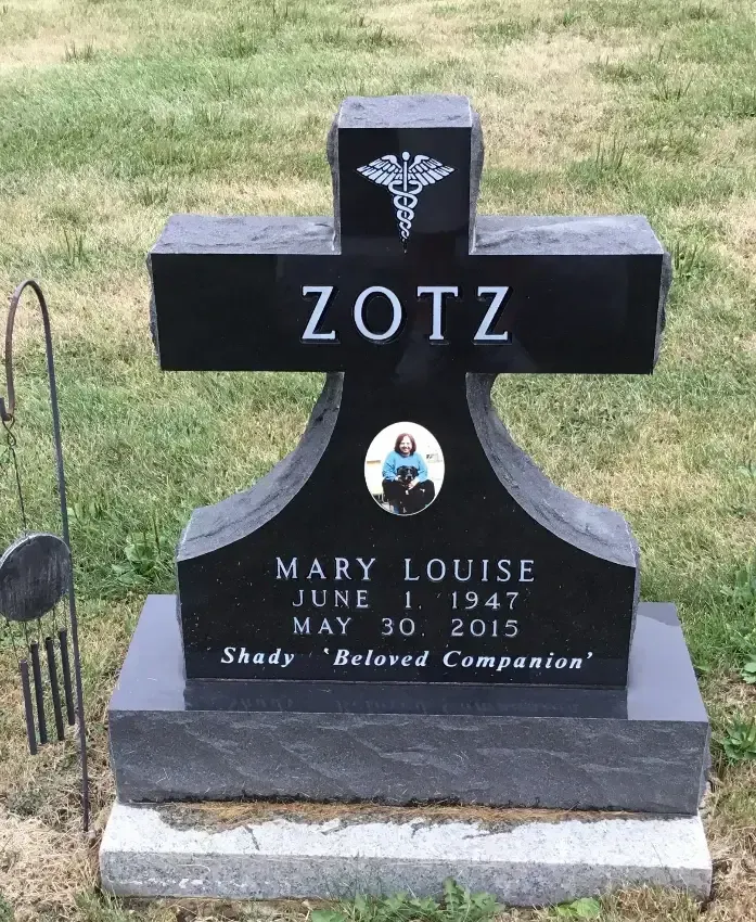 Black gravestone with cross, engraved ZOTZ and Mary Louise, standing on grass.