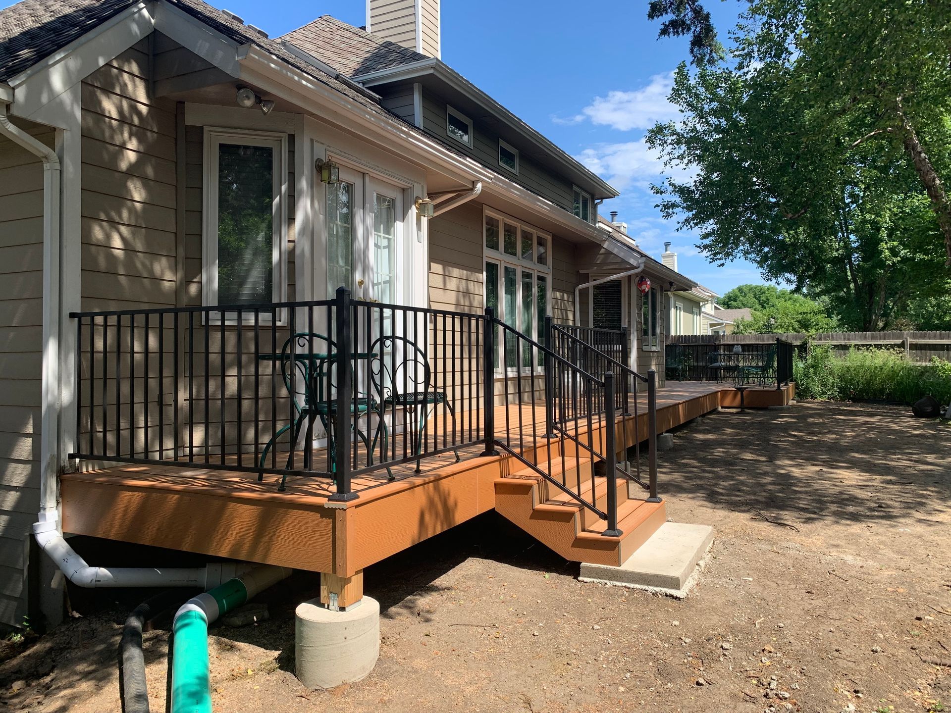 Apartment porch with black railing, steps, and two chairs beside a stone exterior under a blue sky
