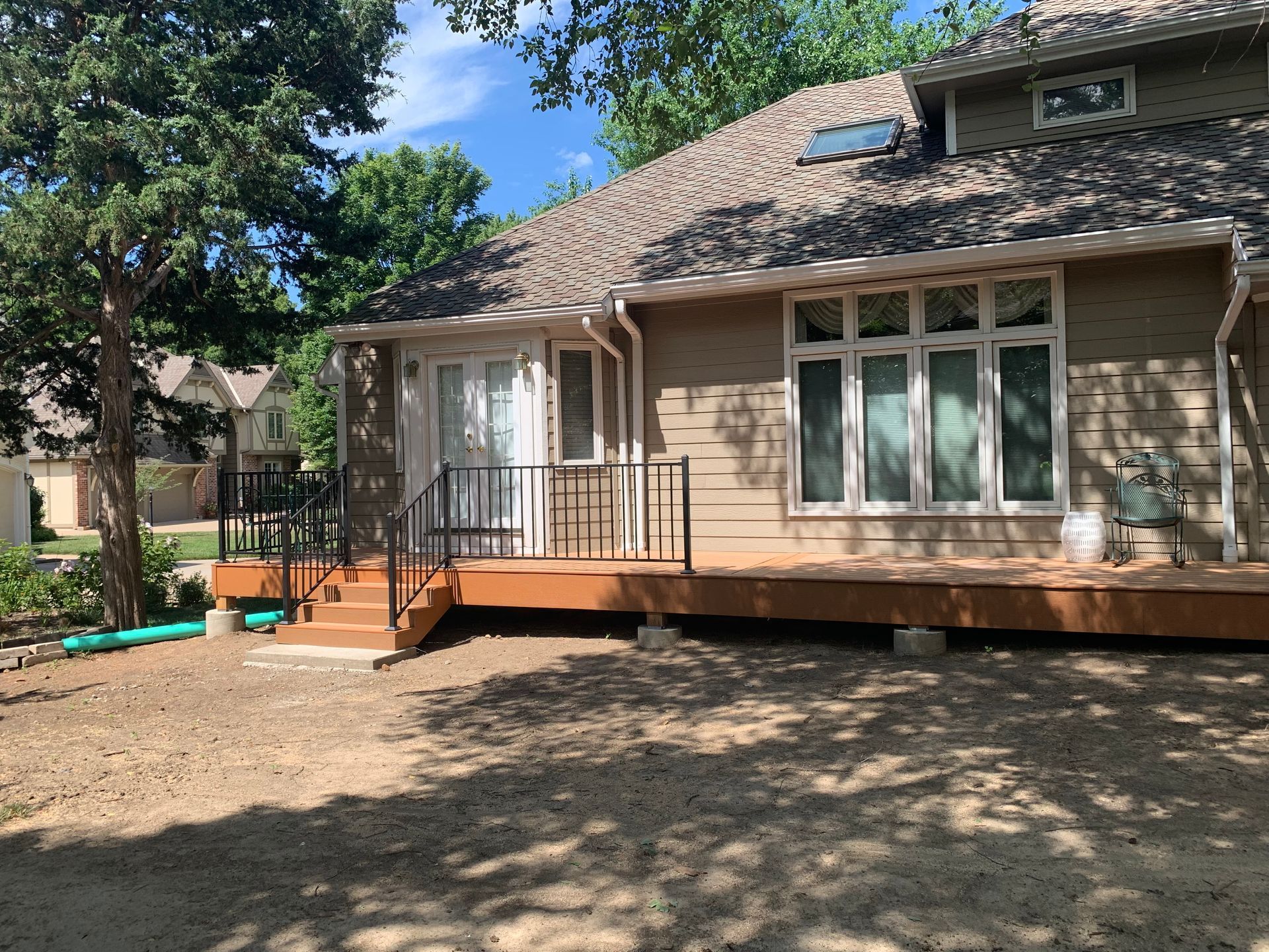Backyard view of a house with a raised wooden deck, steps, and large windows under trees
