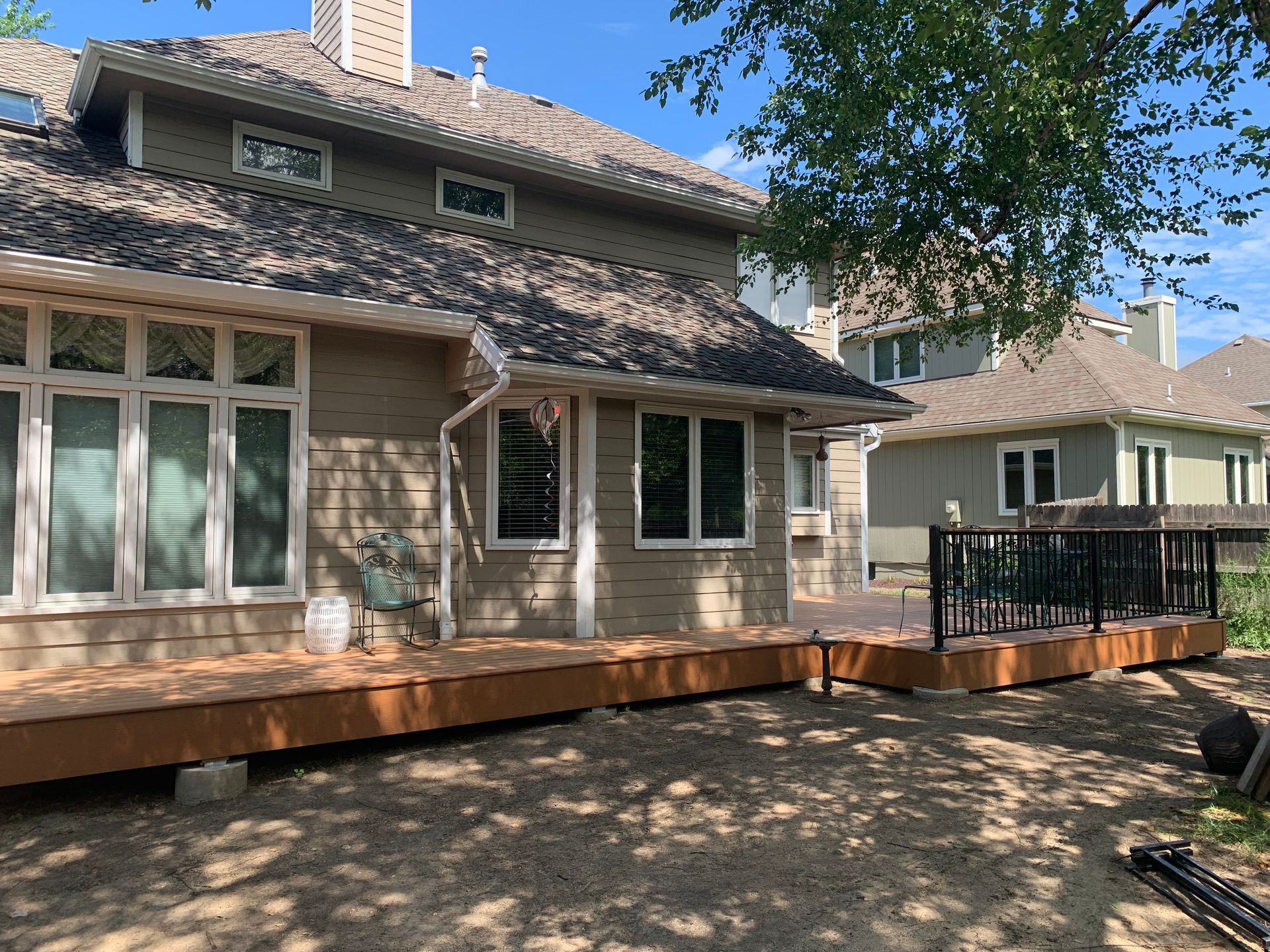 Backyard patio with a stone house, large windows, and a wooden deck under a sunny sky