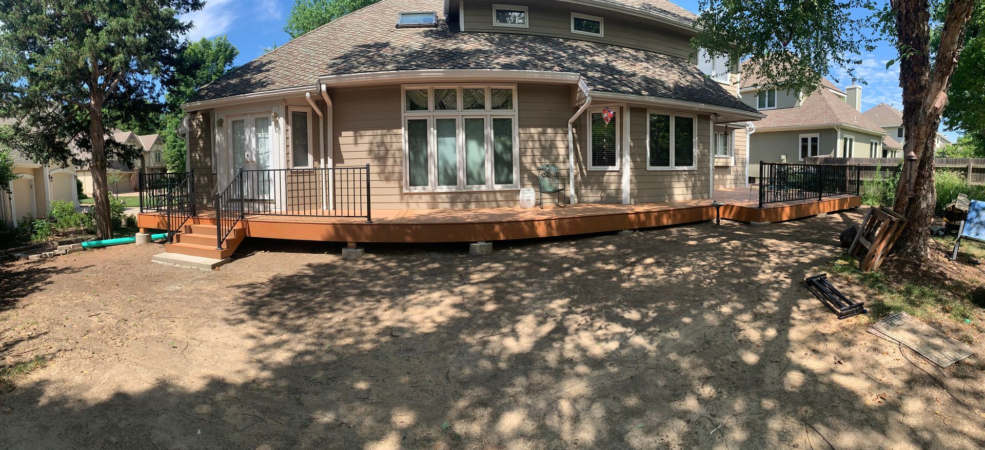 Wide front view of a rustic house with a wooden deck and trees in a sandy yard
