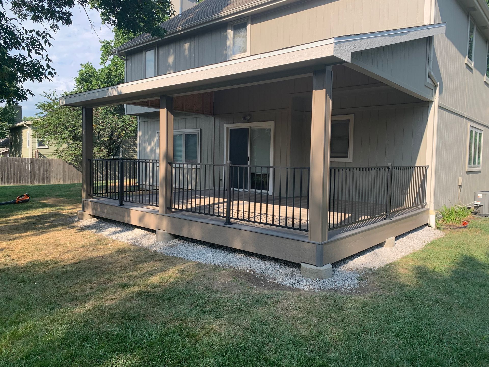 Gray house with a covered front porch, black railing, and a small grassy yard.