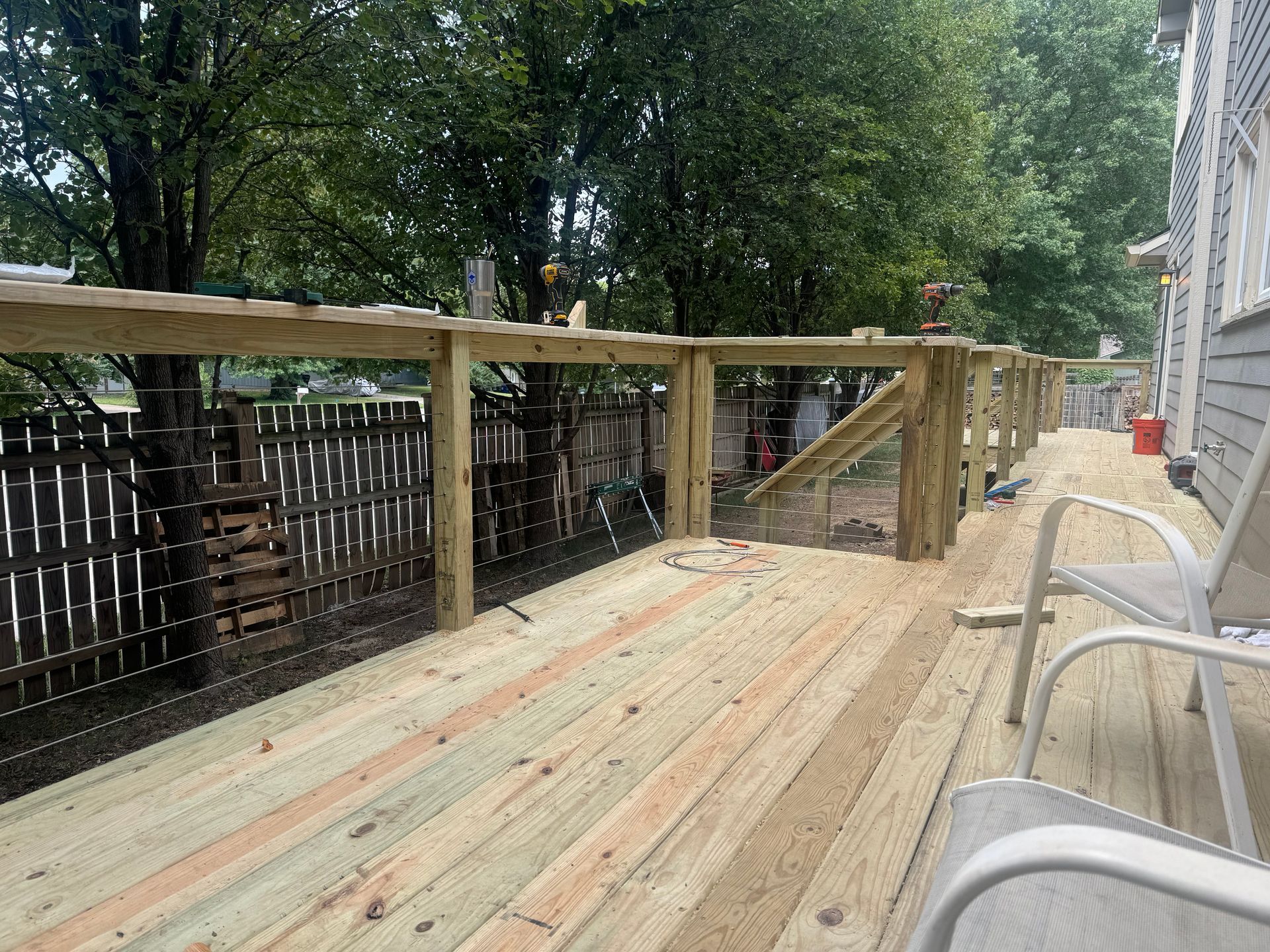 Wooden ramp/deck beside a house with railings, leading toward a tree-lined yard.