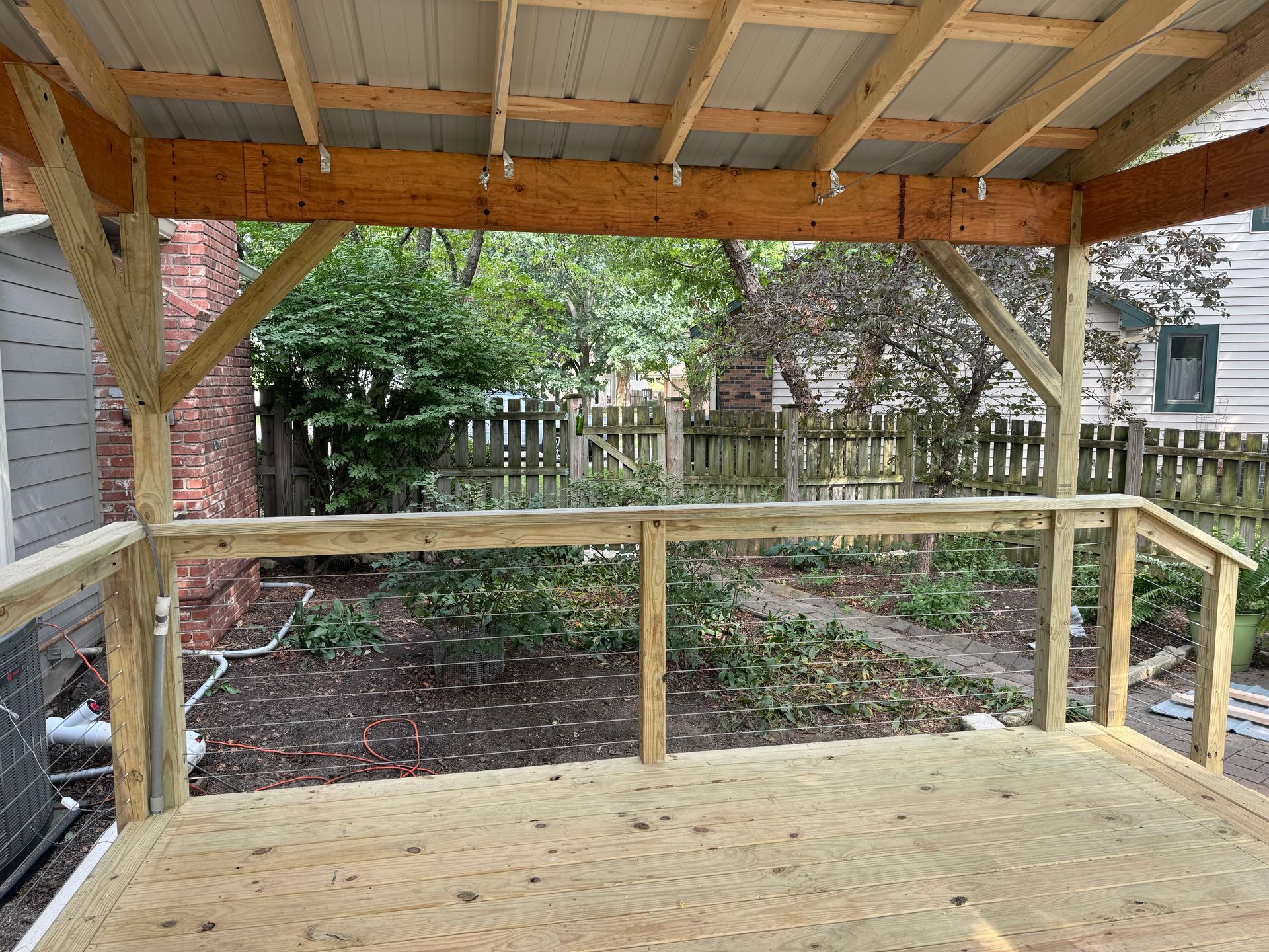 Covered wooden deck overlooking a fenced backyard with trees and a garden path