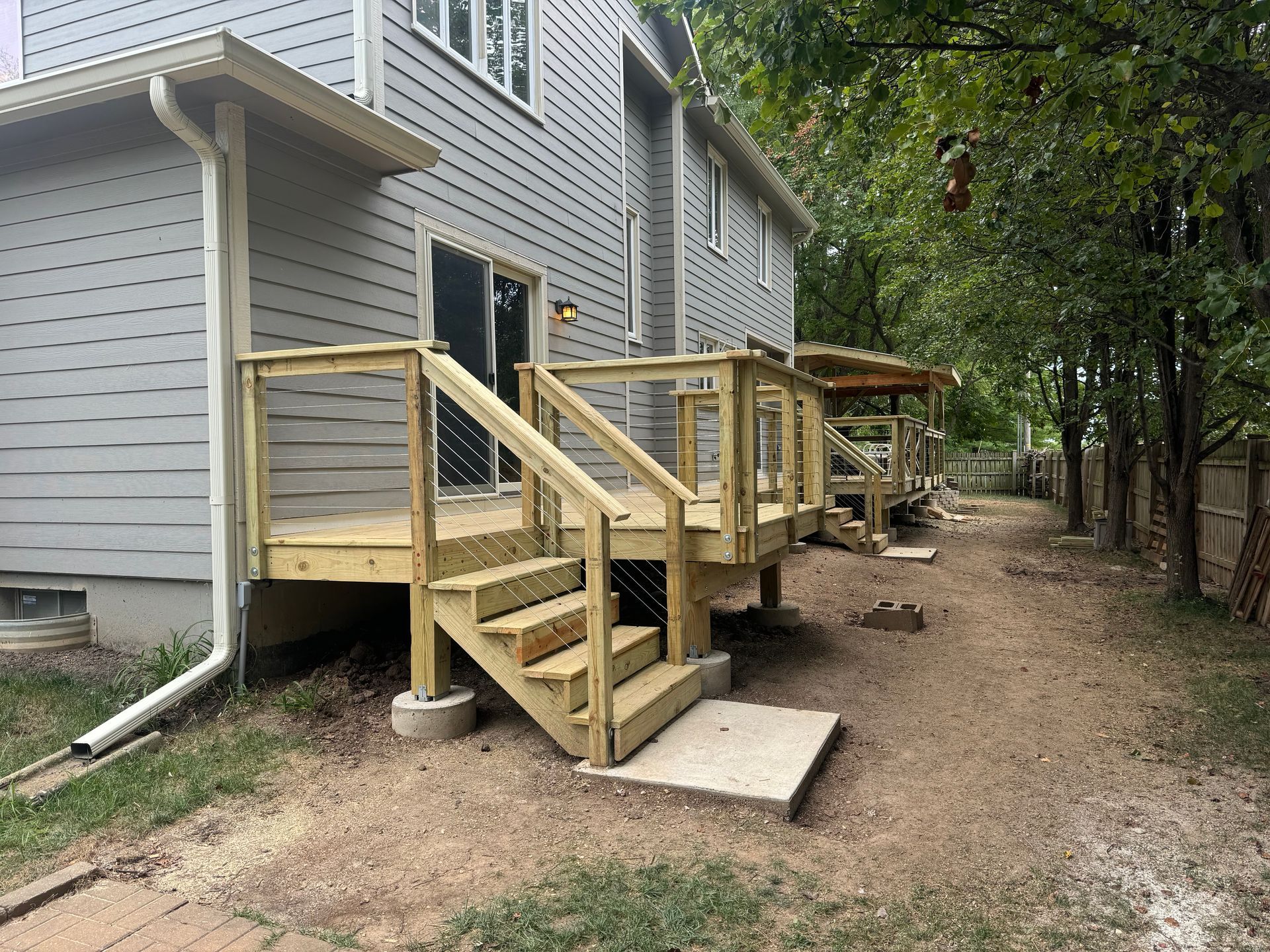 Wooden accessibility ramps and stairs along a gray apartment building beside a dirt path and trees