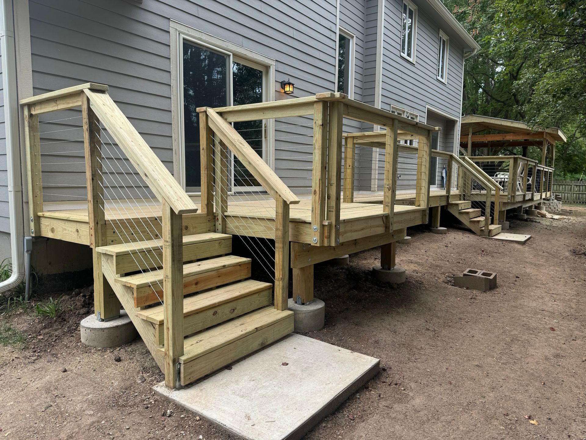 Wooden accessible ramp and stairs leading to a house deck, with concrete supports and unfinished yard.