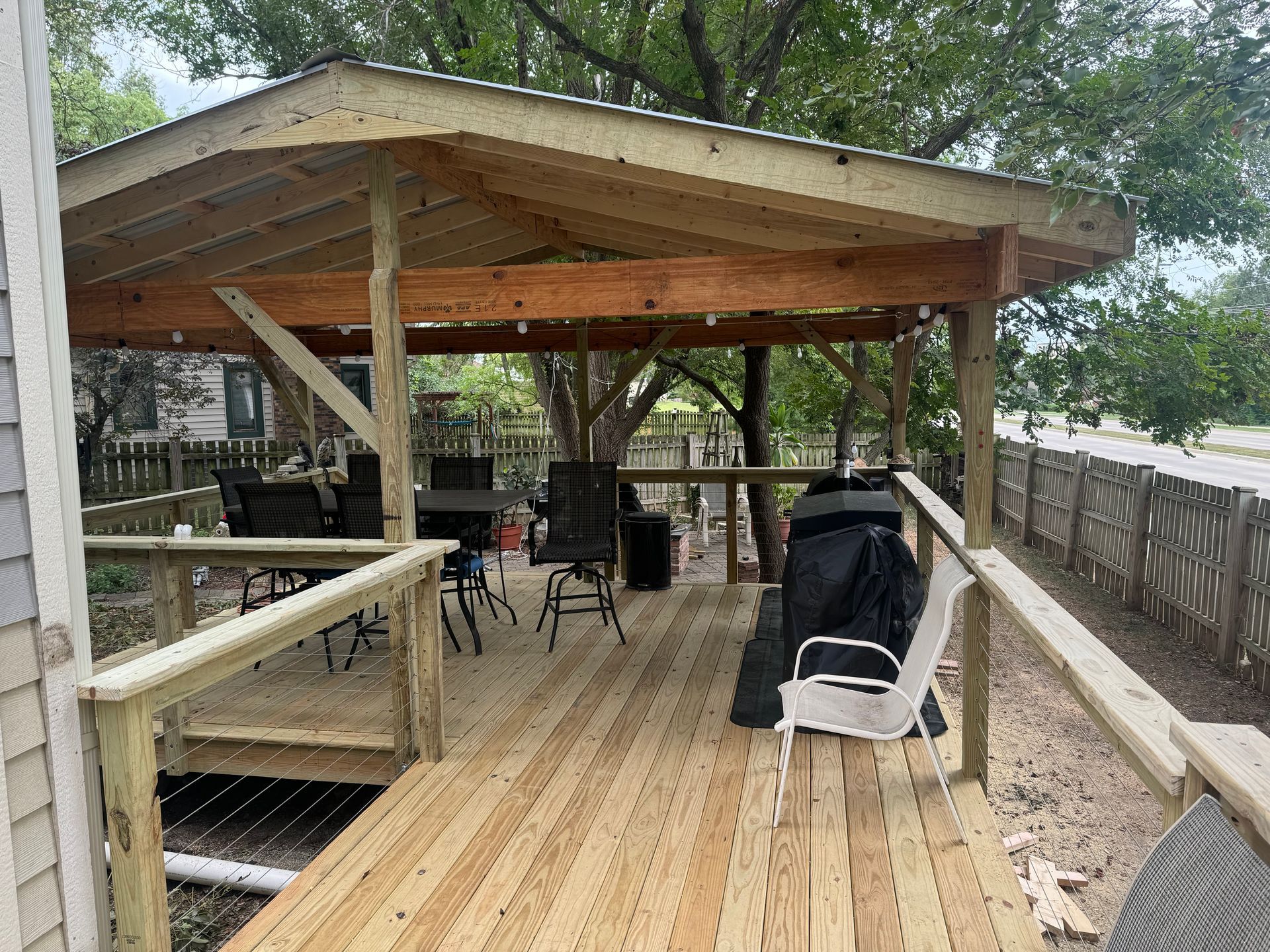 Wooden deck gazebo with railings, patio furniture, and a black grill under a sloped roof outdoors