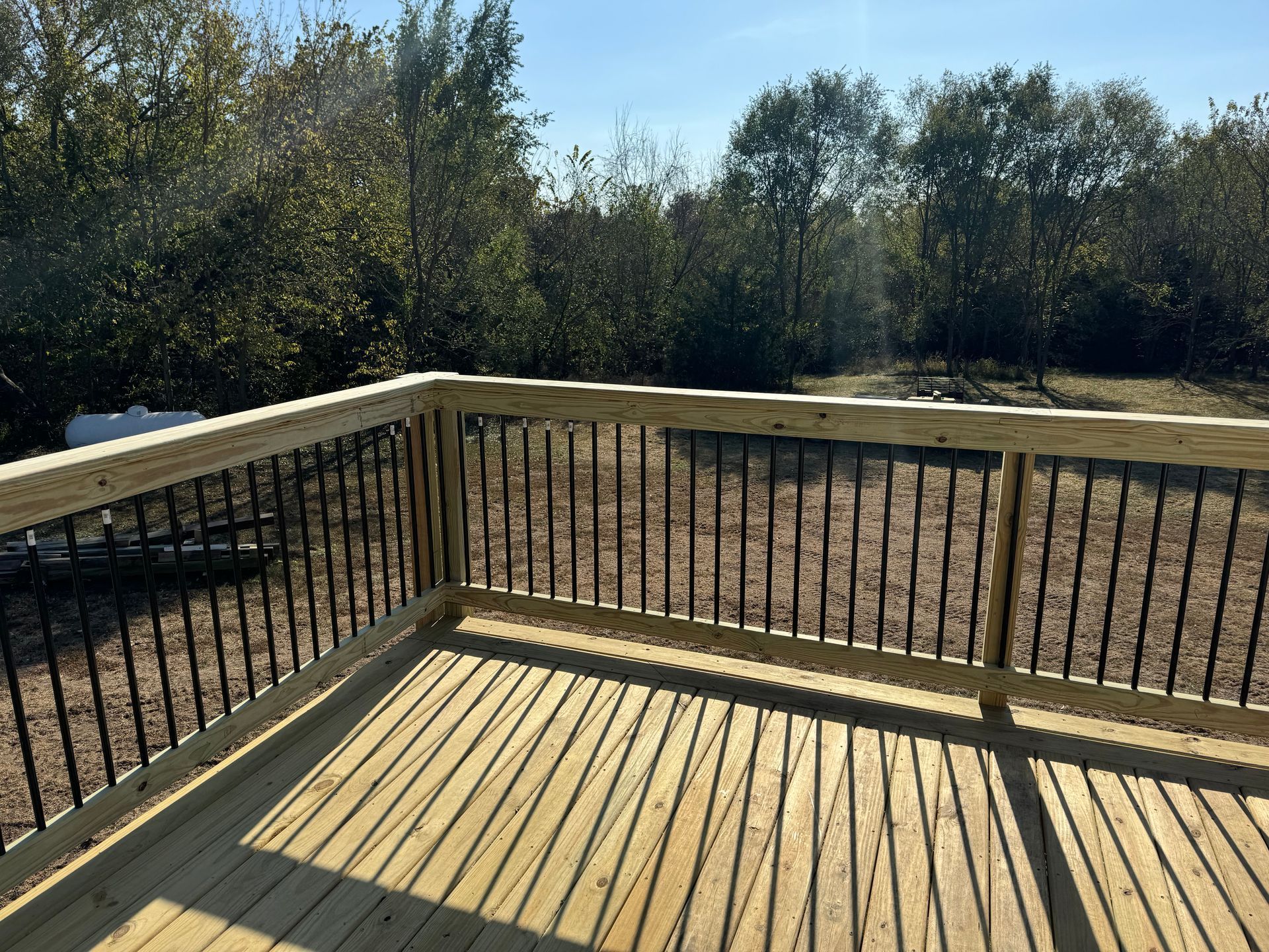 Wooden deck with black railing overlooking a wooded backyard in daylight