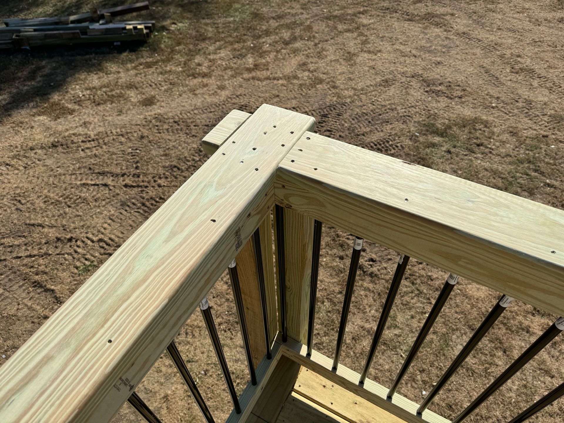 Wooden deck railing corner with black metal balusters and dirt ground below