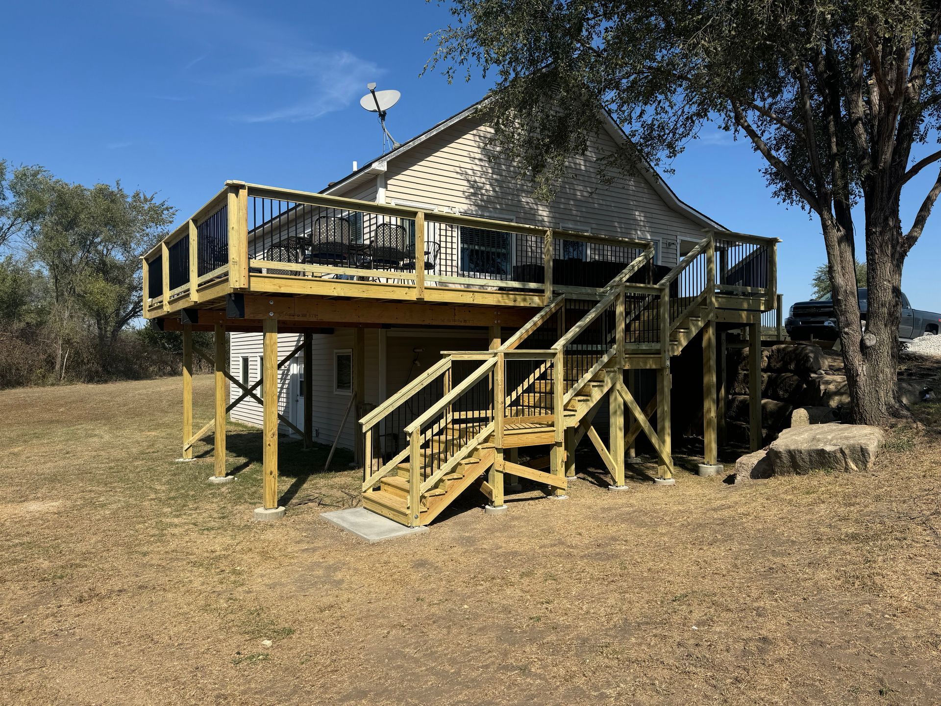 Elevated house with a wooden deck and stairs on a dry grassy hillside under a blue sky