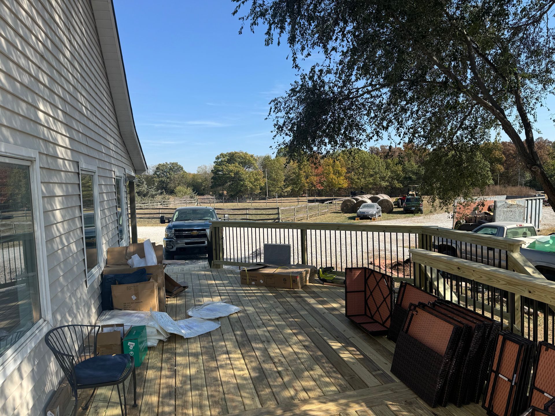 Wooden deck beside a house with stacked chairs, a table, and a parked truck in the driveway.