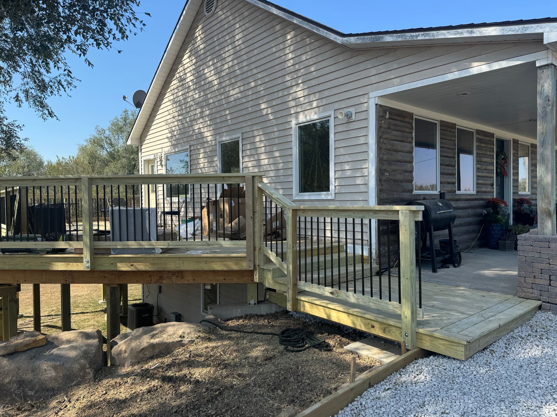 Backyard deck ramp and wooden porch attached to a beige house with black railings and gravel path