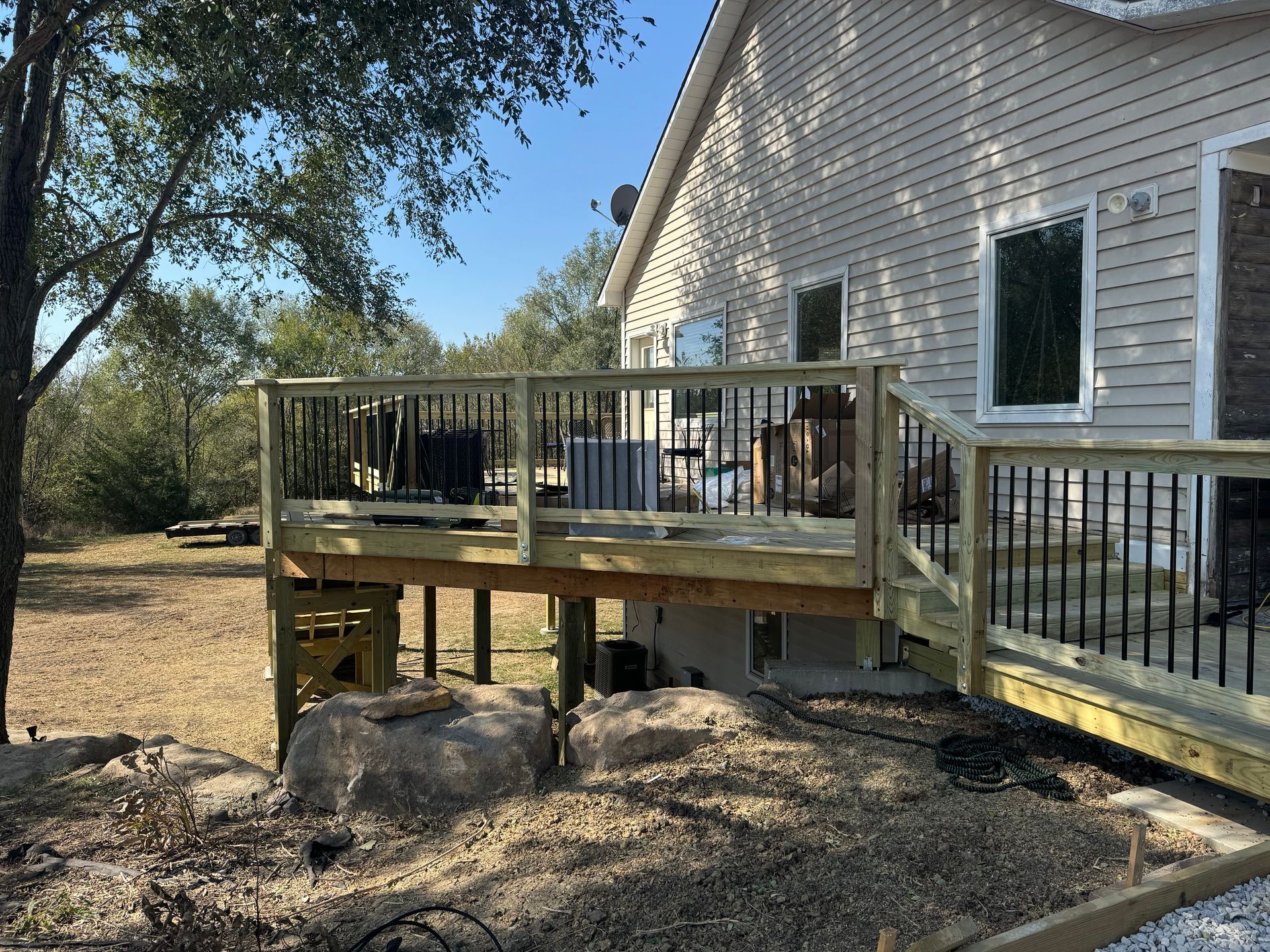 Wooden deck beside a beige house, with railing and patio furniture in a leafy backyard