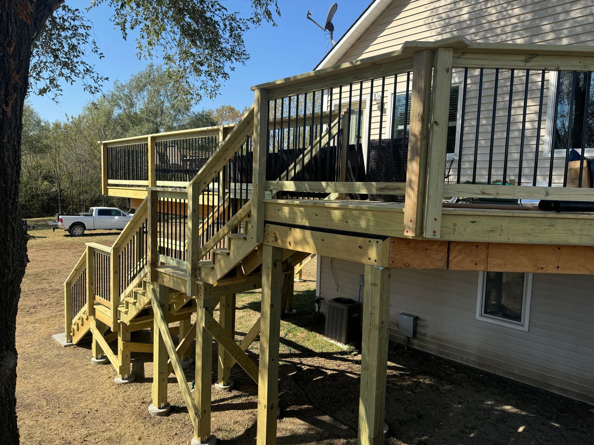 Wooden backyard deck with stairs attached to a house, under a tree in a grassy yard