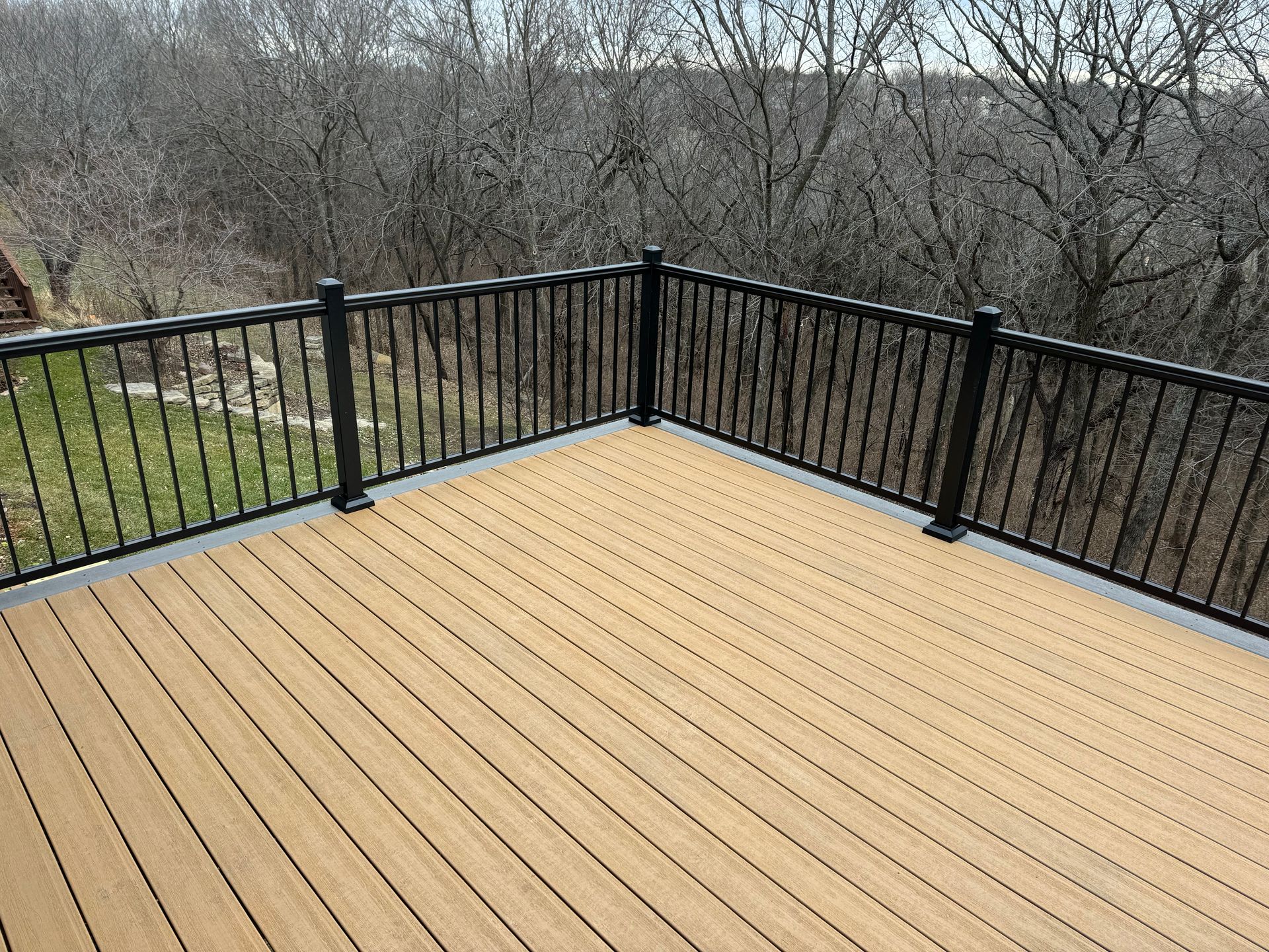 Wooden deck with black railing overlooking leafless trees and a grassy yard