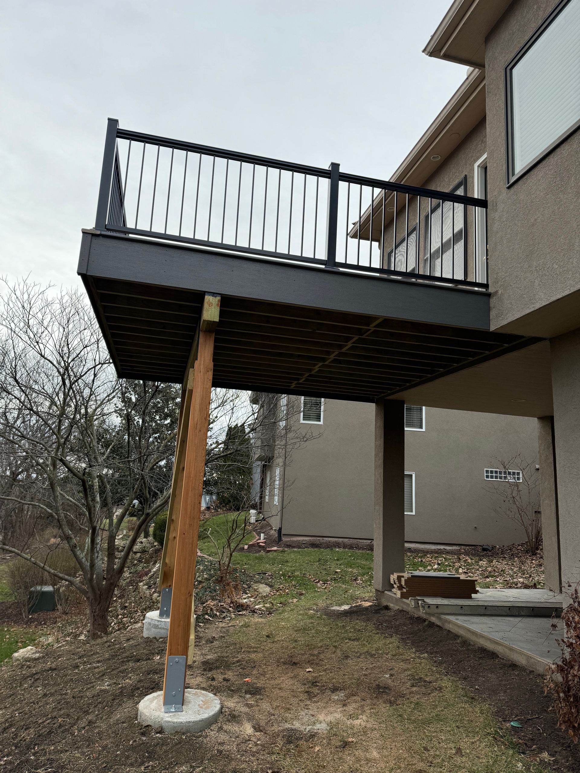 House deck on wooden support posts over a yard with trees and bare ground
