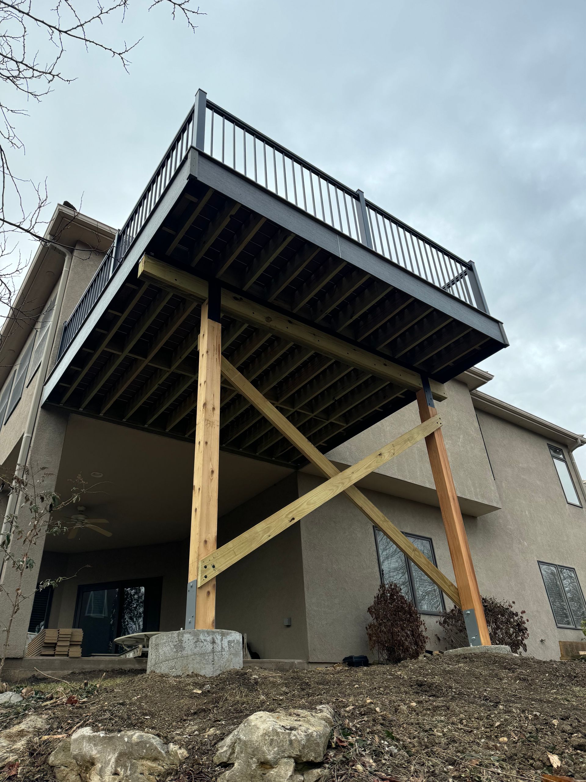 Raised wooden deck attached to a house, supported by diagonal braces on a rocky slope.