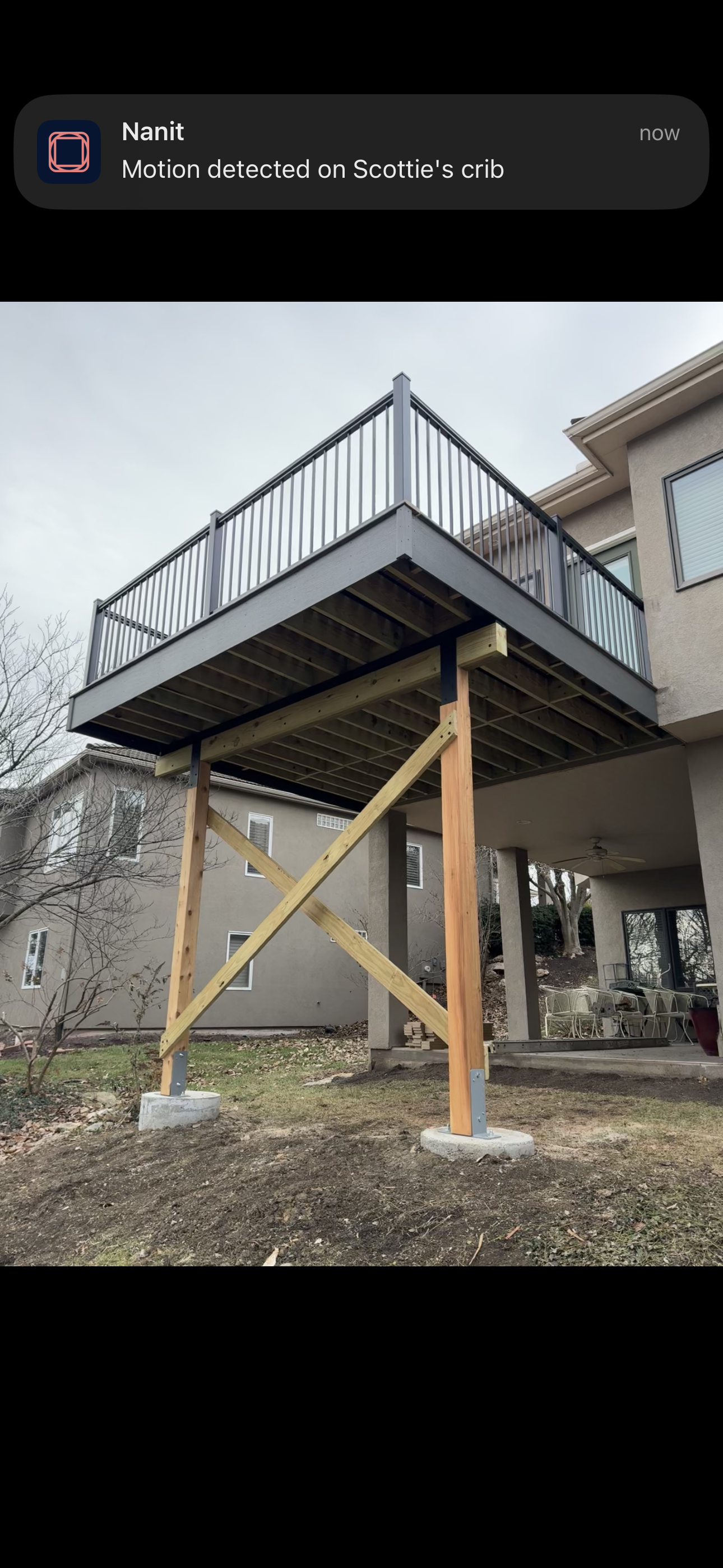 Patio deck under construction with wooden support posts and metal railing on a house exterior