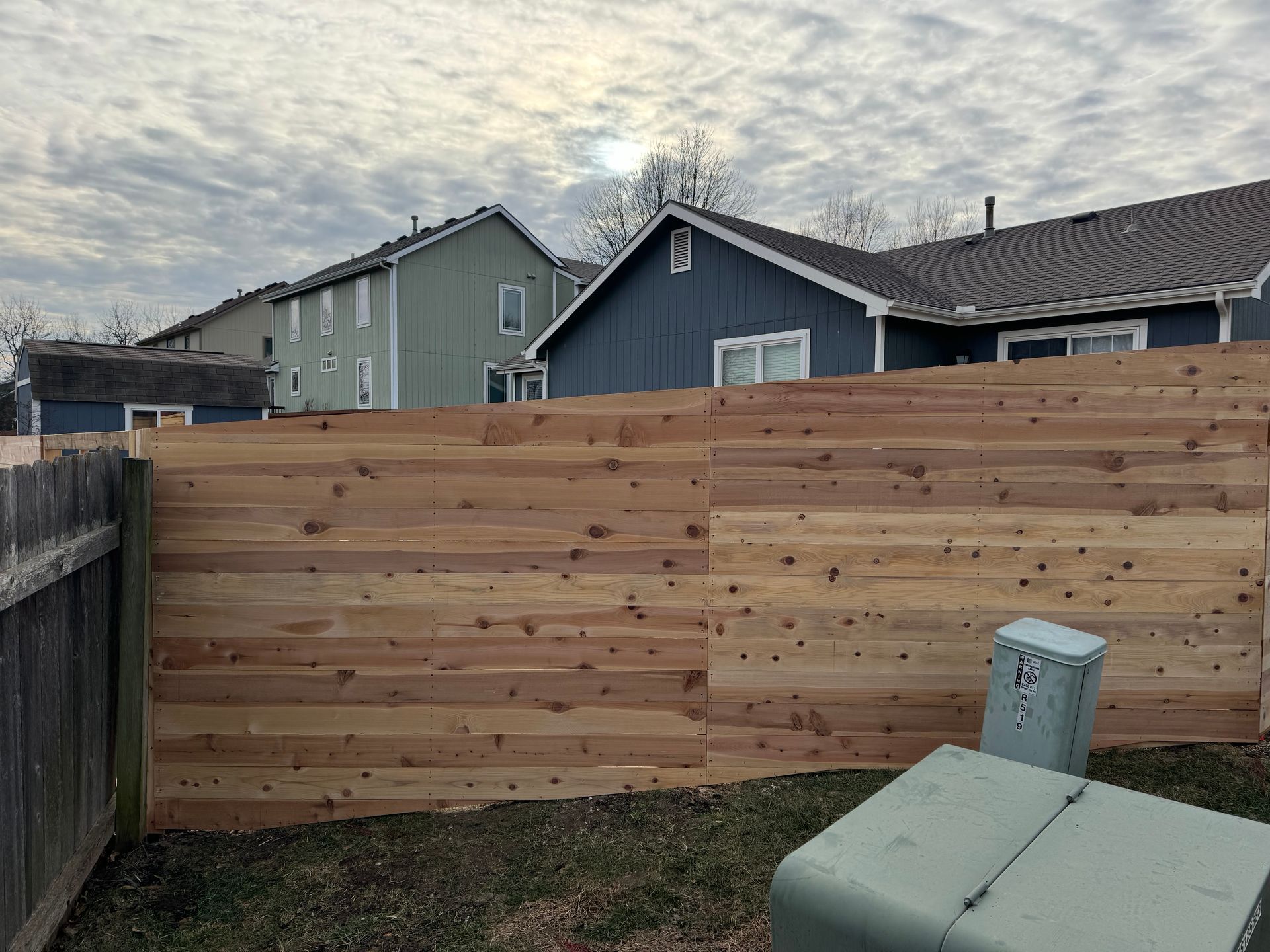 New wooden privacy fence along a backyard, with houses and a cloudy sky in the background