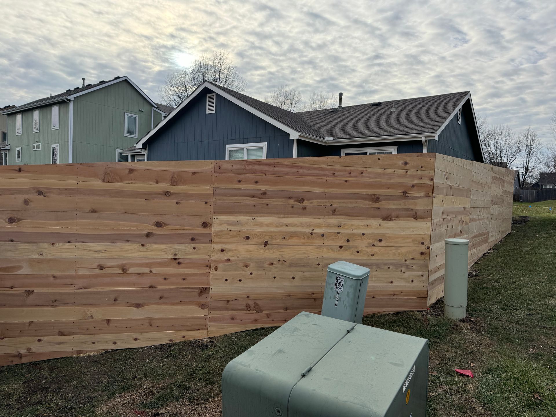 Wooden privacy fence beside a house under construction, with utility boxes in the foreground.