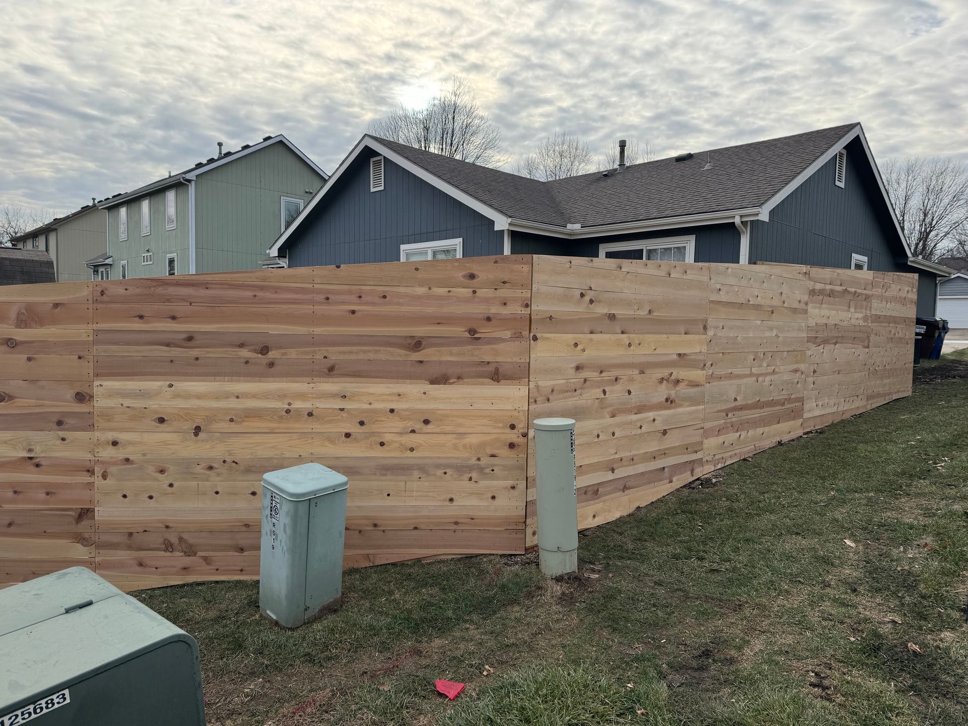 Wooden privacy fence around a yard beside a gray house under a cloudy sky.