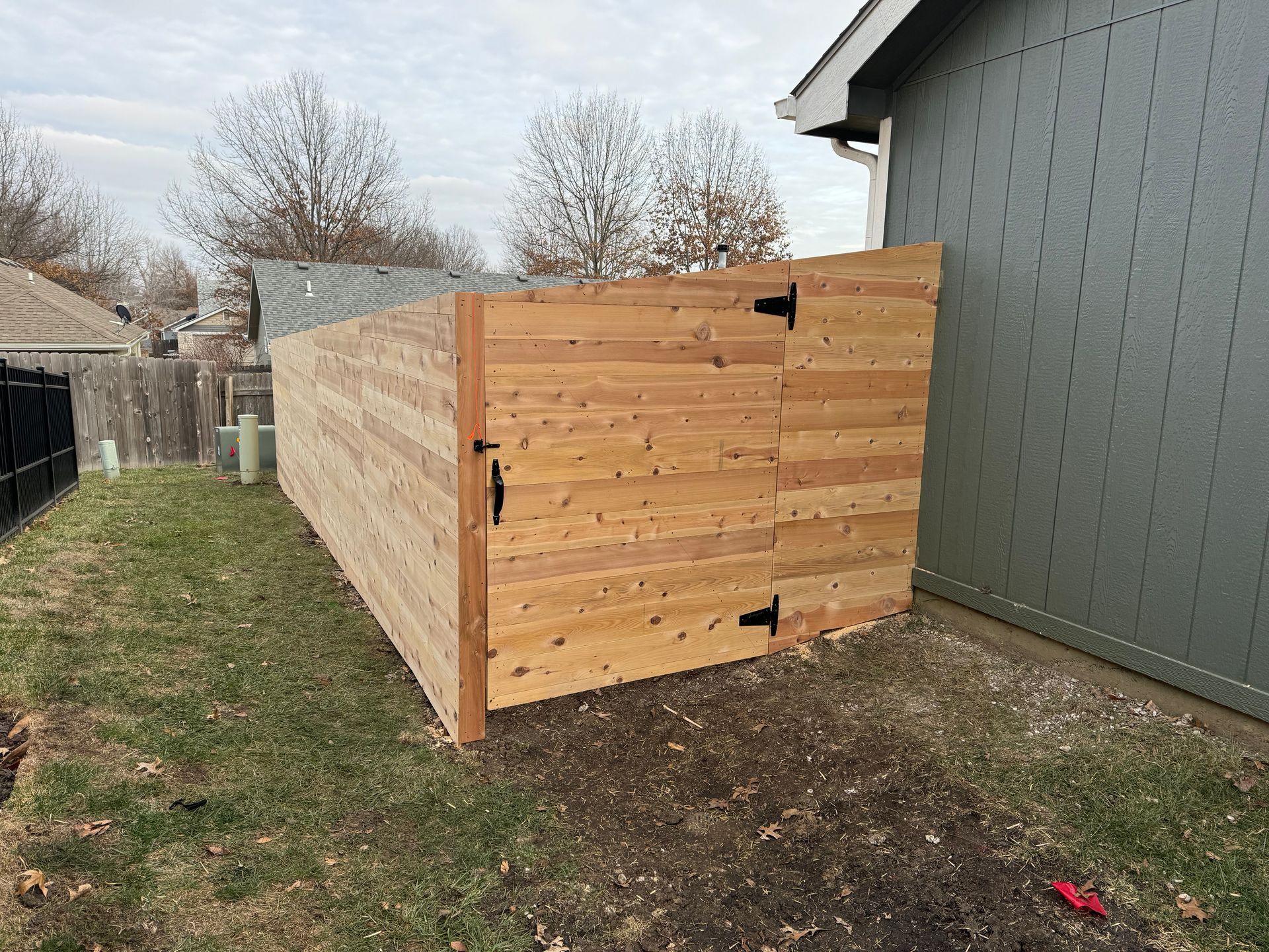 Wooden storage shed beside a gray house in a backyard, viewed from the front corner.