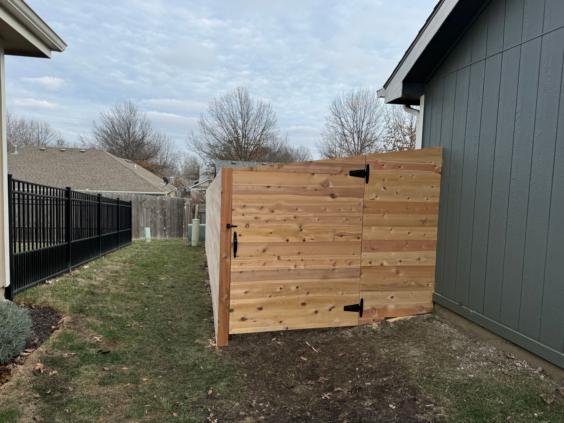 Wooden animal pen or storage box beside a gray house in a narrow backyard area