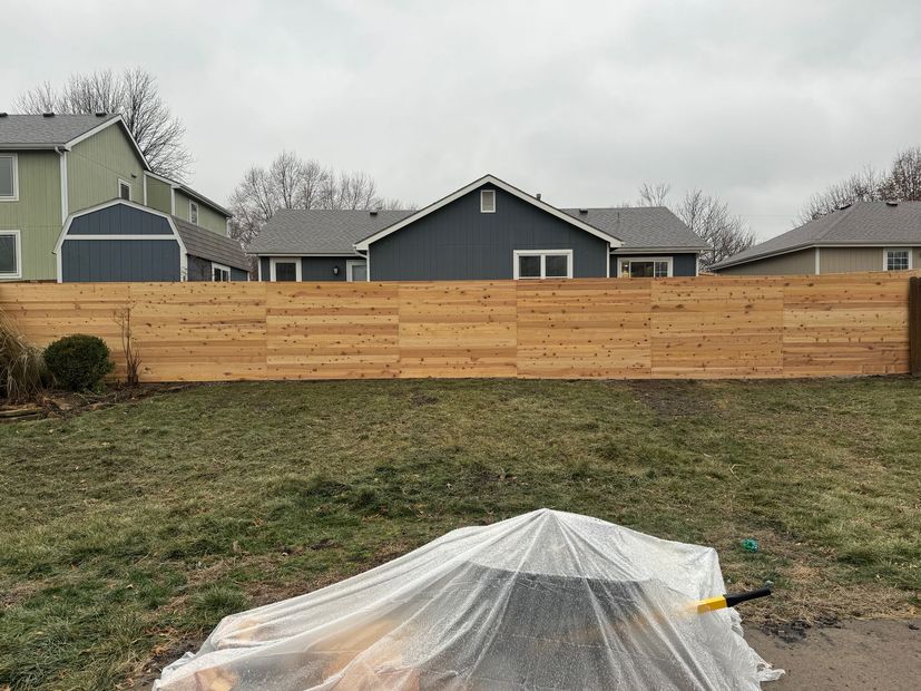 Backyard garden bed covered with clear plastic, in front of a wooden privacy fence and houses