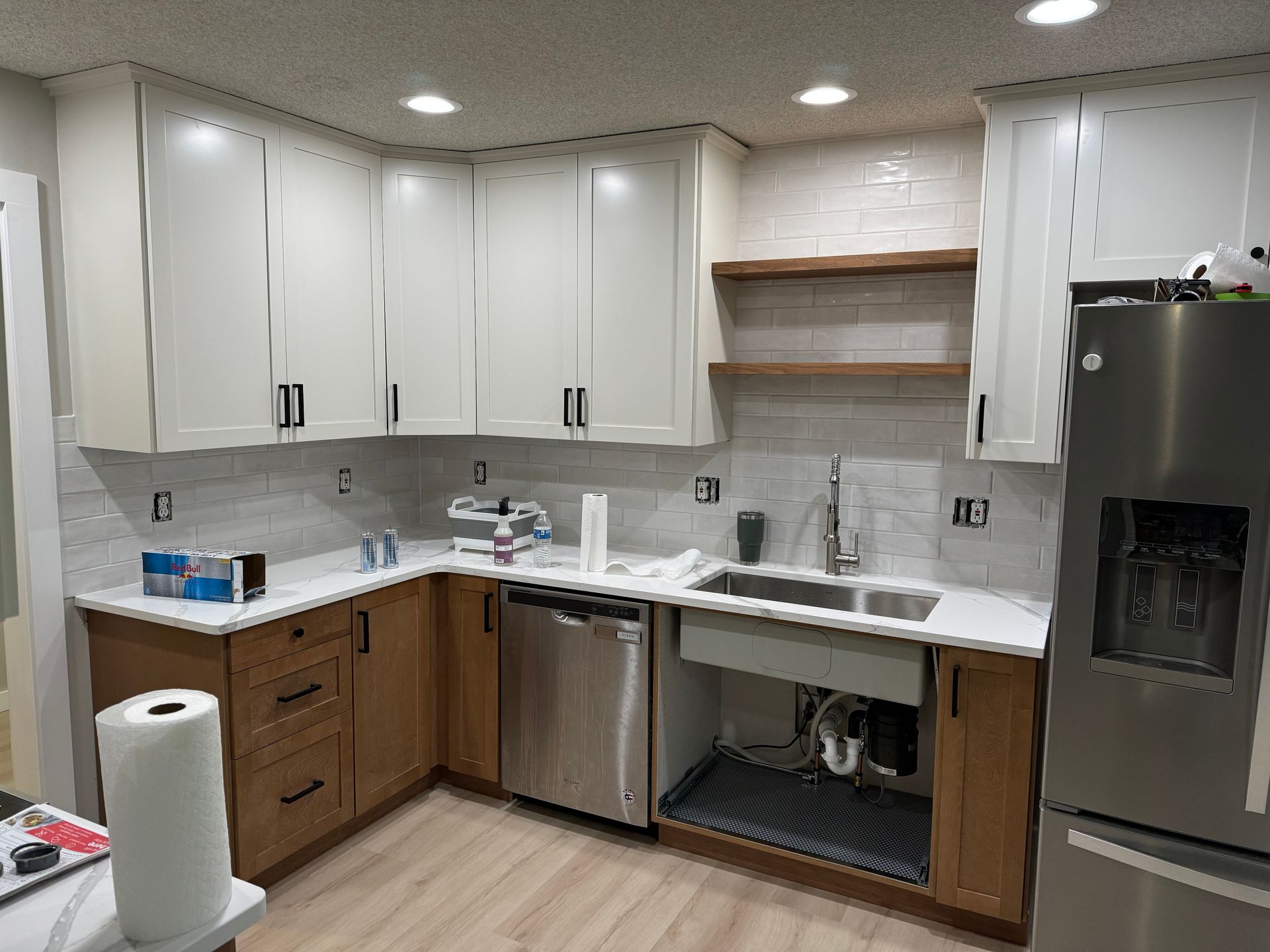 Modern kitchen with white cabinets, wood lower cabinets, stainless steel fridge, and a double sink with open shelving