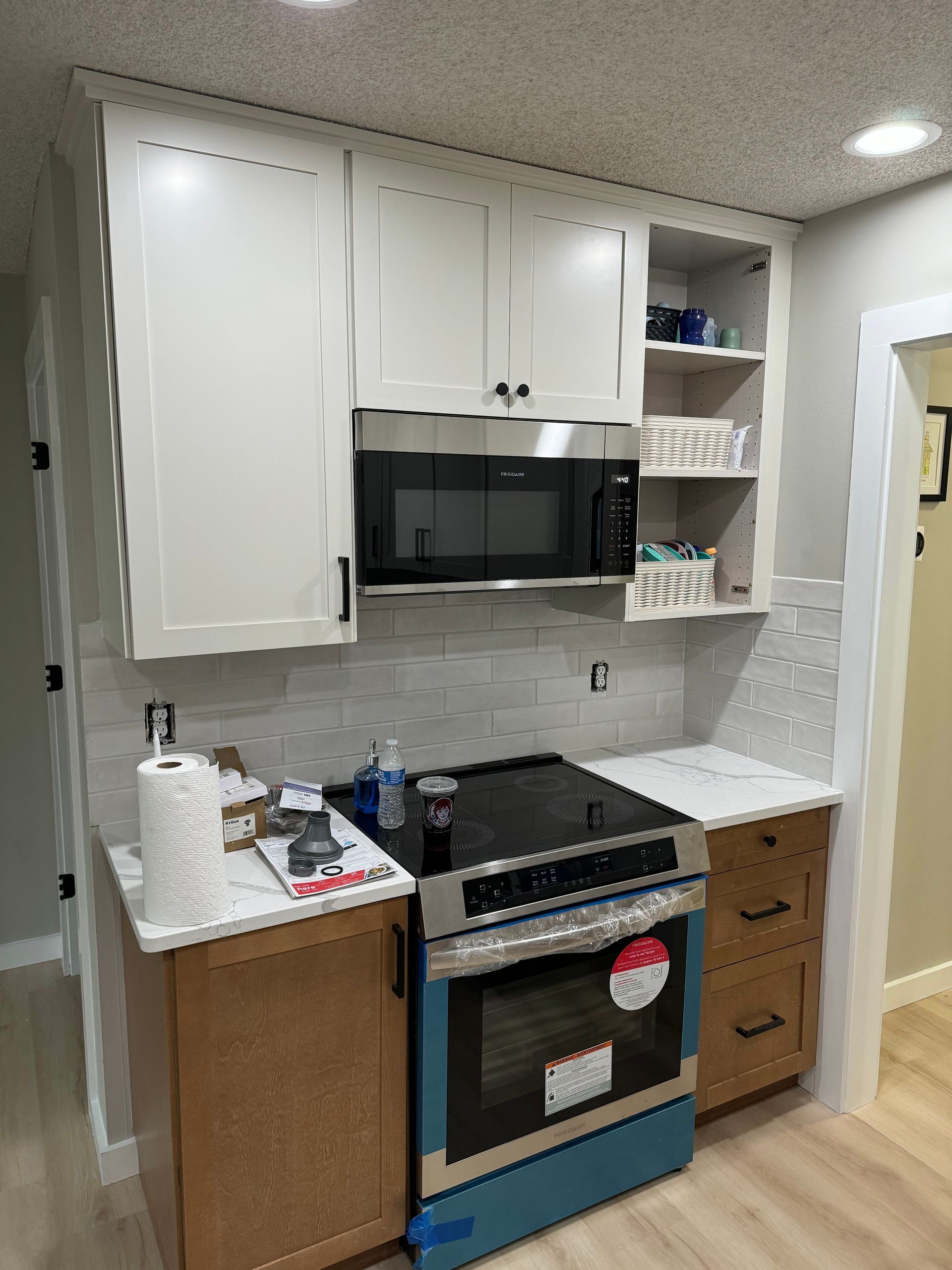 Small kitchen with white cabinets, black stove, and marble-pattern backsplash in a compact apartment