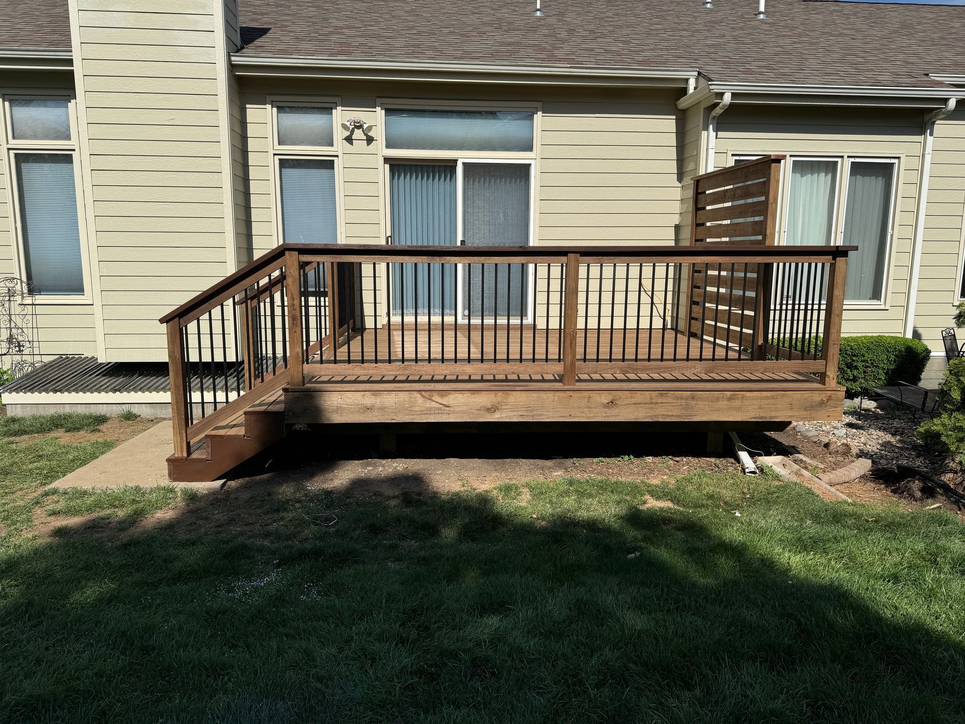 Wooden backyard deck with railing and steps attached to a beige house.