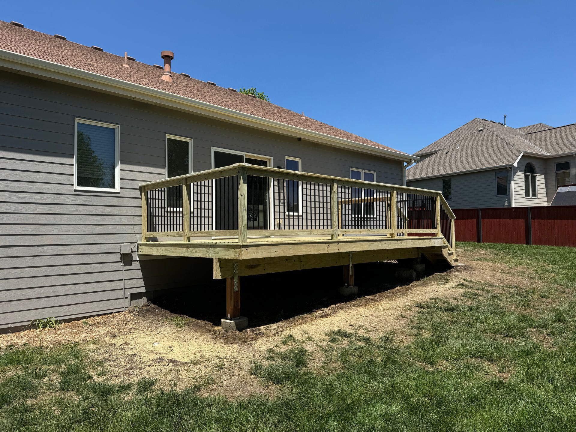 Raised wooden deck attached to a beige house in a grassy backyard on a sunny day