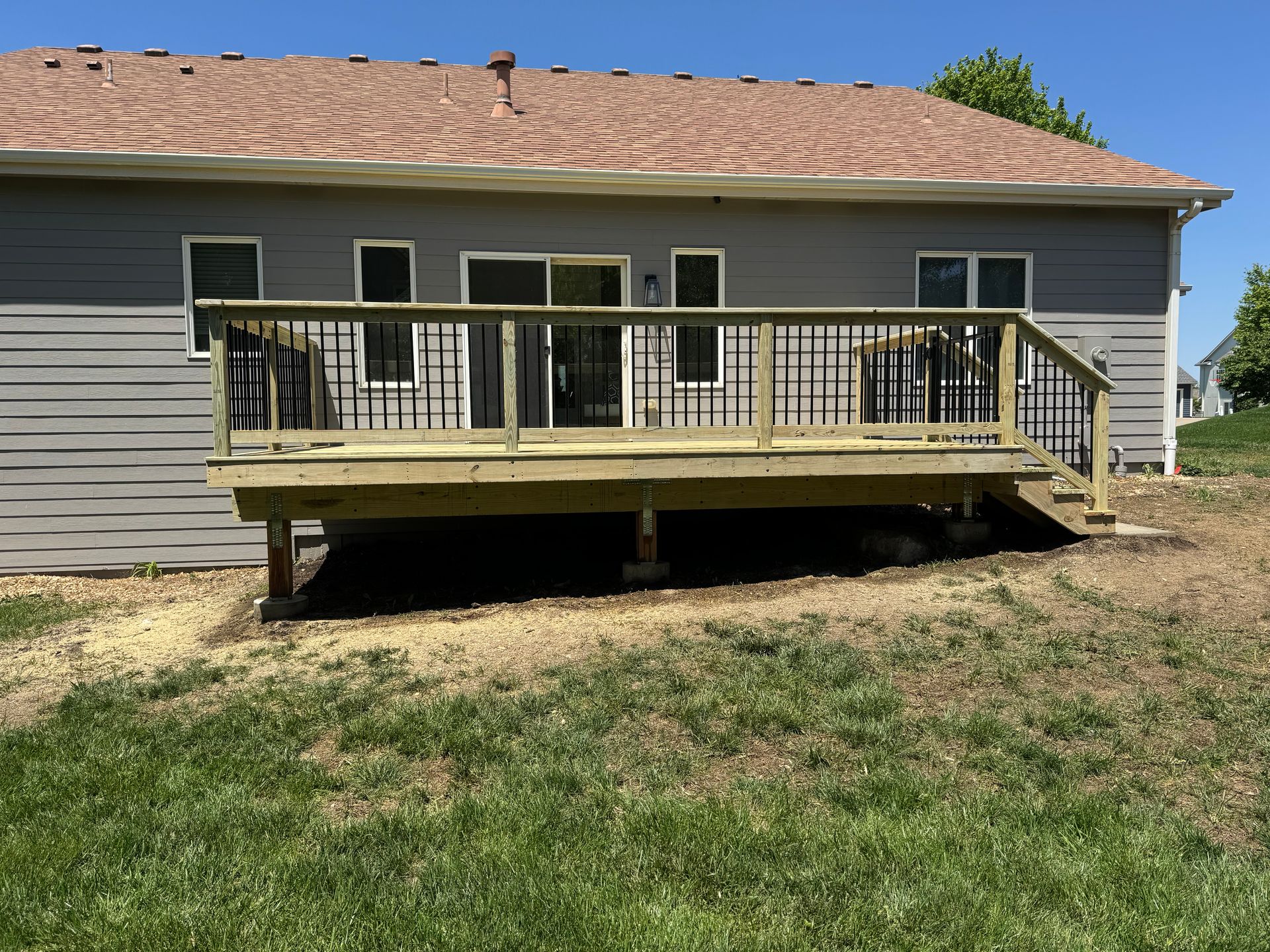 Backyard wooden deck with railing attached to a gray house on a grassy lawn