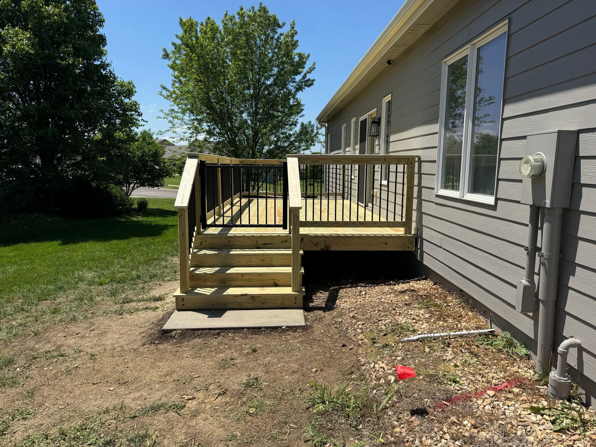 Backyard wooden deck with steps beside a gray house and grassy lawn