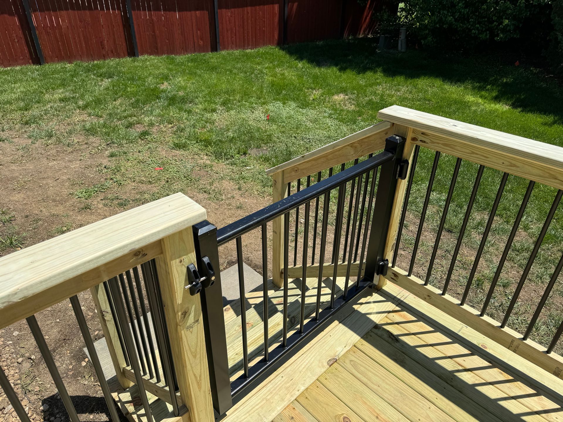 Wooden deck stairs with black metal railing leading to a grassy backyard
