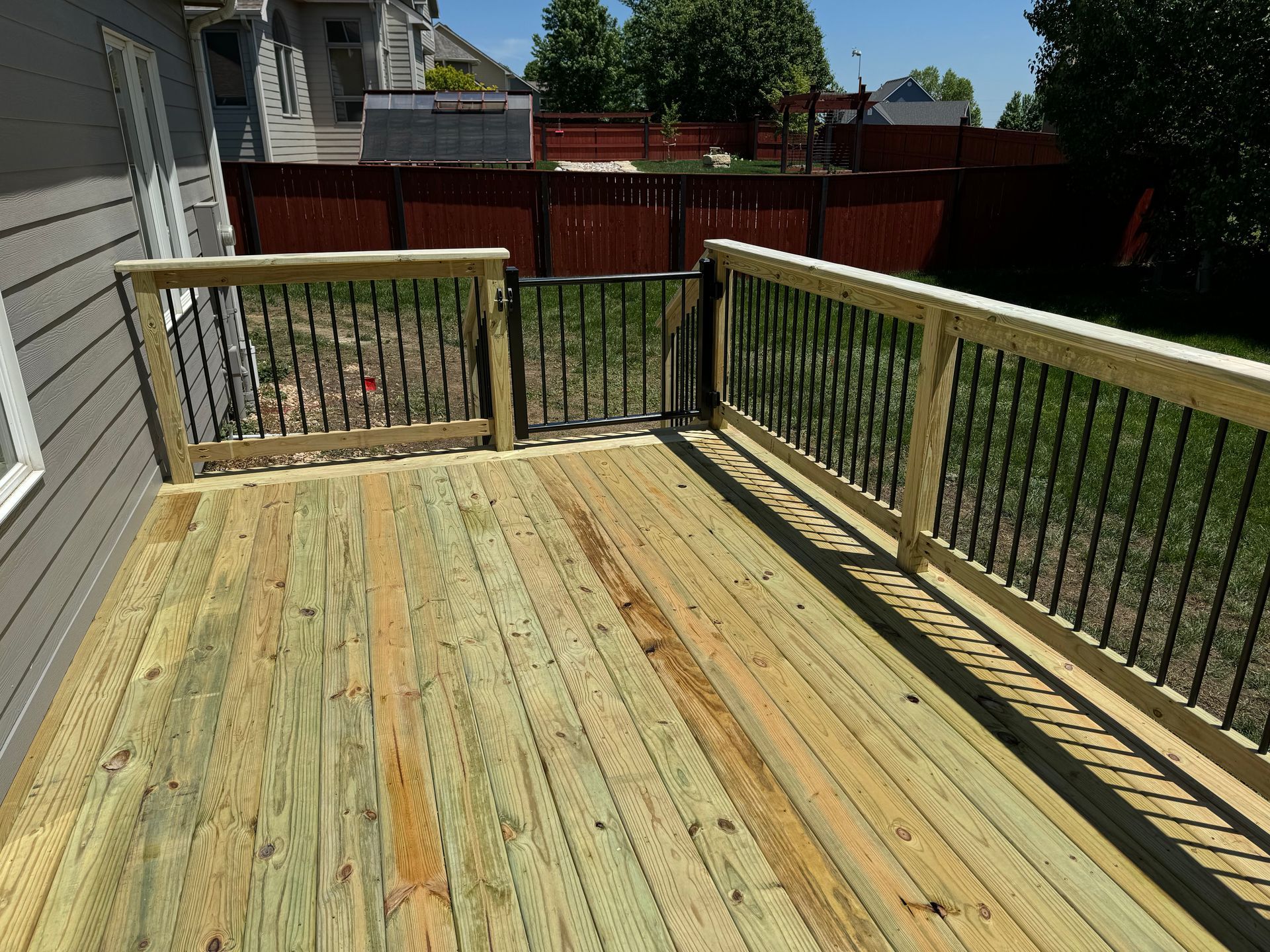 Wooden deck with railings and steps overlooking a backyard fence and trees