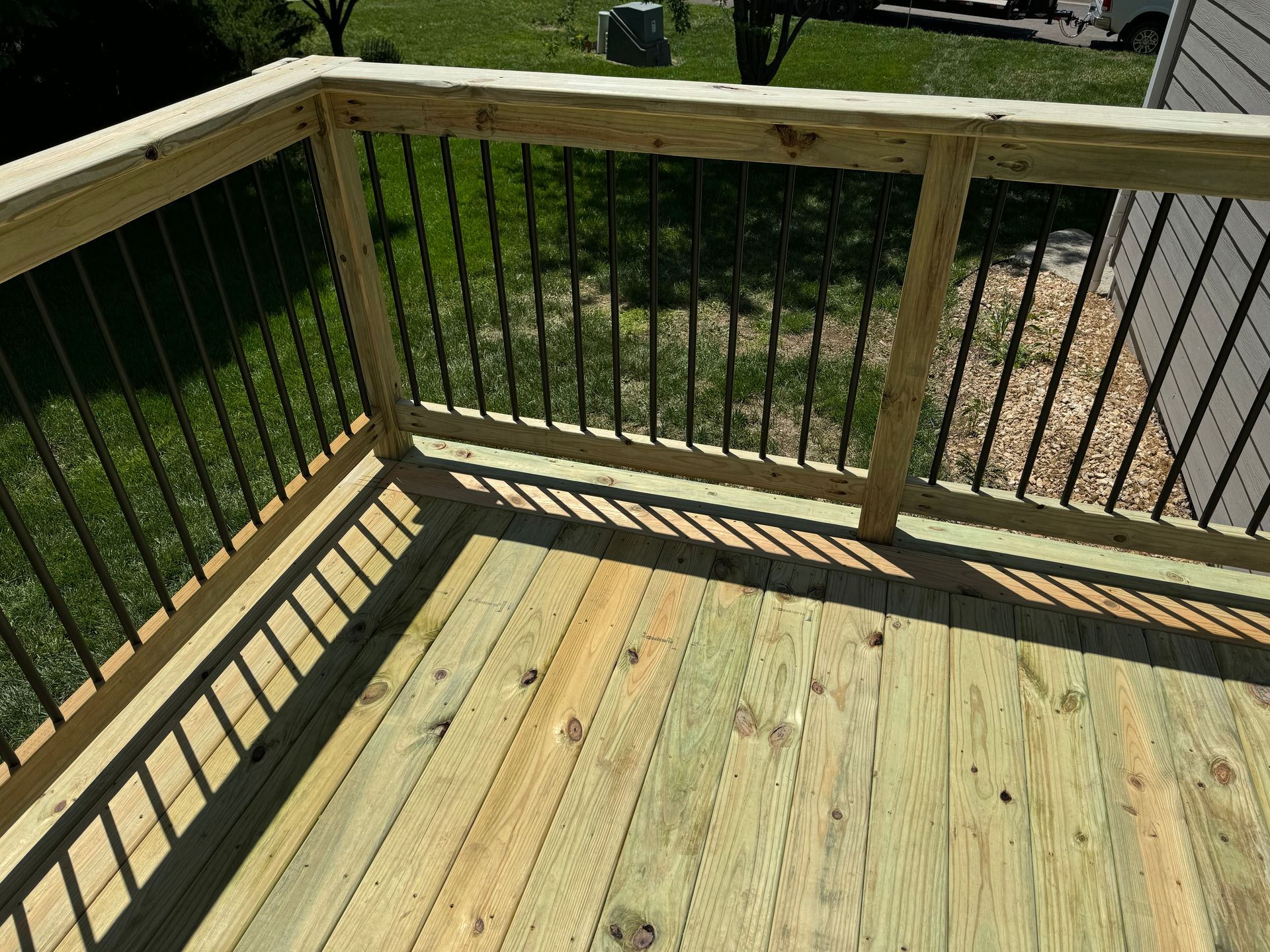 Wooden deck with black railing overlooking a grassy yard in sunlight