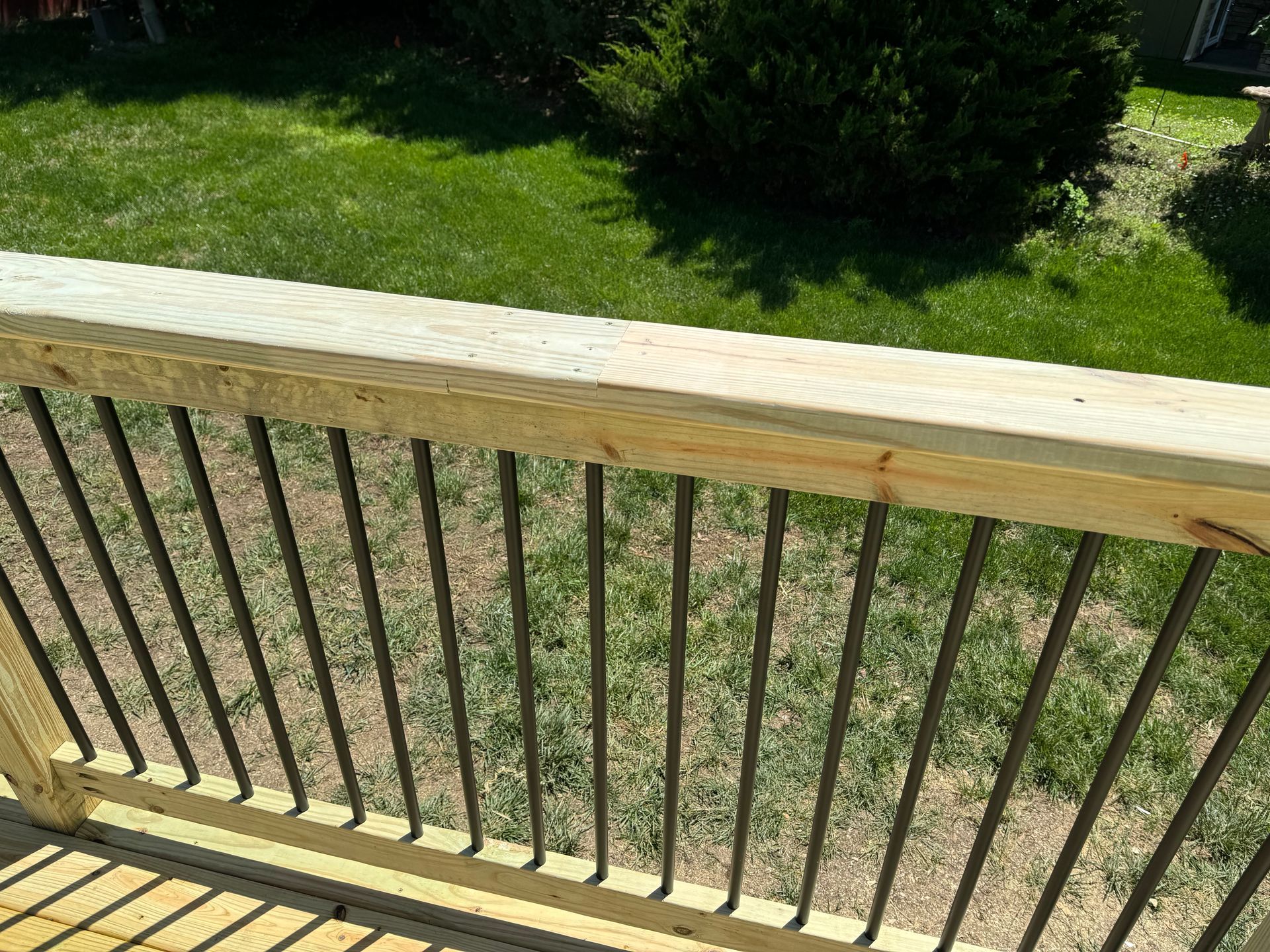 Wooden deck railing with black metal balusters overlooking a grassy backyard