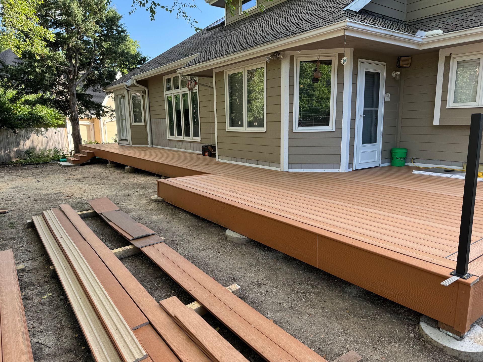 Wooden deck under construction beside a tan house, with boards laid out in the foreground.