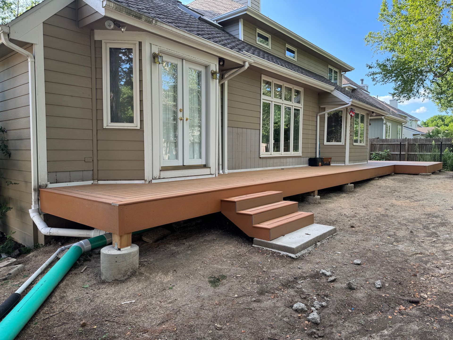 Wooden backyard deck with steps beside a beige house under construction on a gravel yard