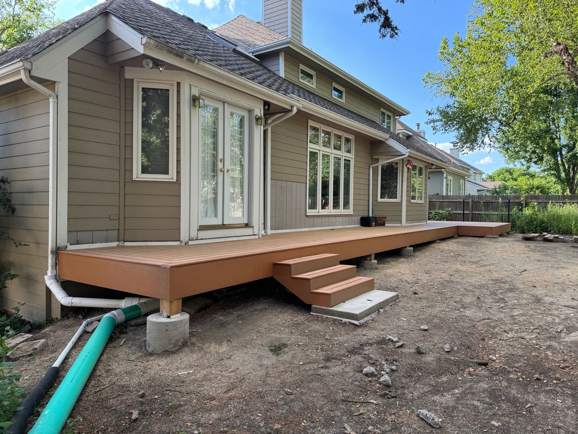Backyard deck with steps and sliding glass doors on a beige house, beside a gravel yard