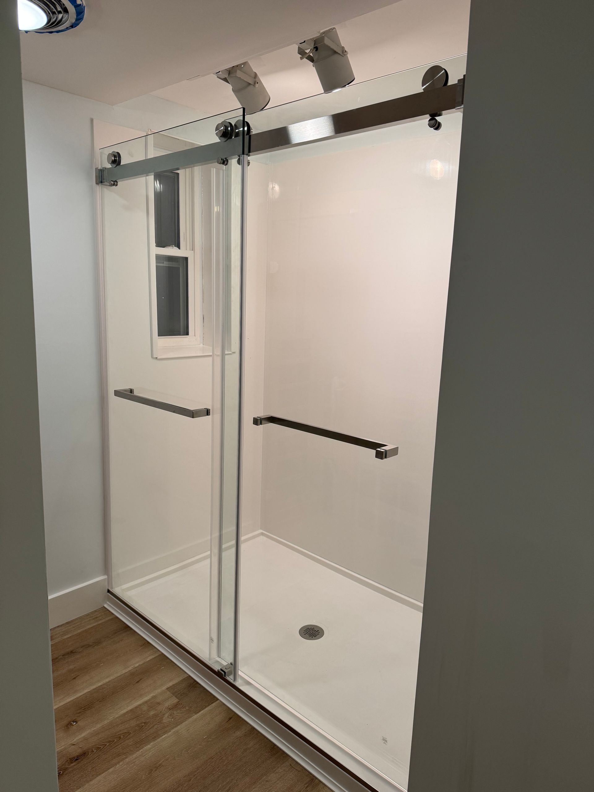 Glass shower enclosure with sliding doors, chrome rail, and white bathroom walls