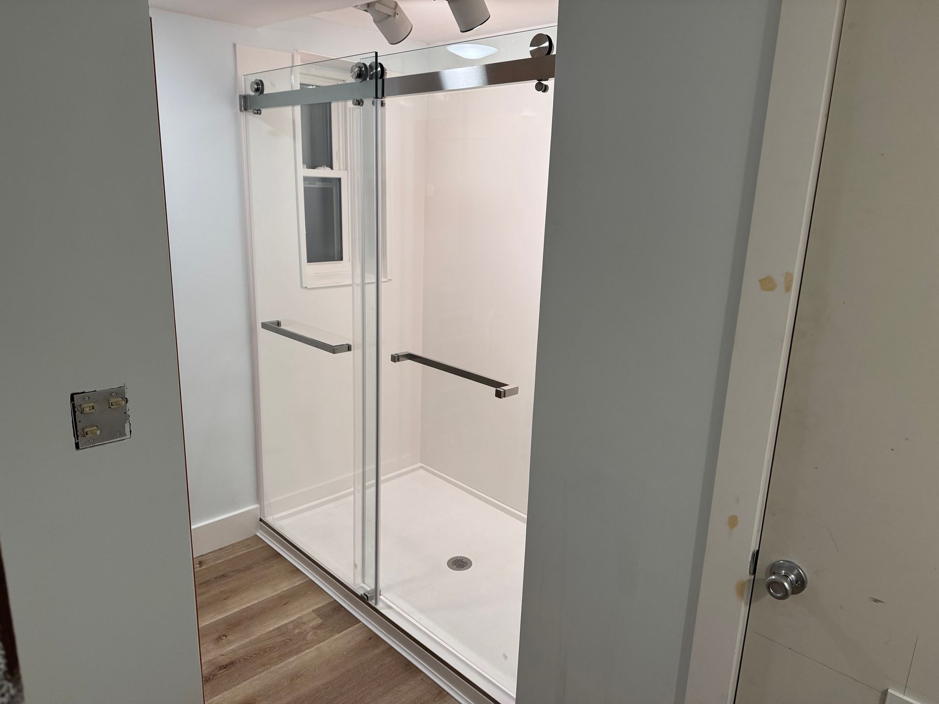 White bathroom with a glass sliding shower enclosure and wood-look tile floor