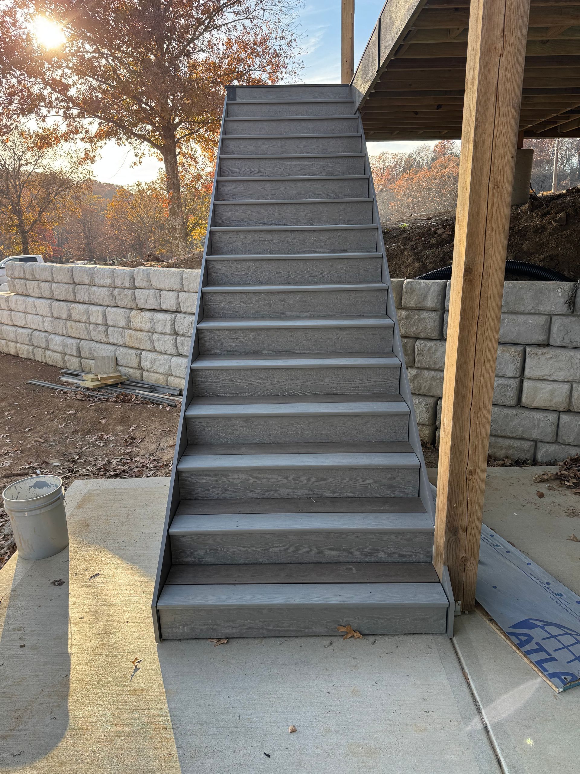 Outdoor concrete staircase beside a building, with a stone retaining wall and trees in the background.