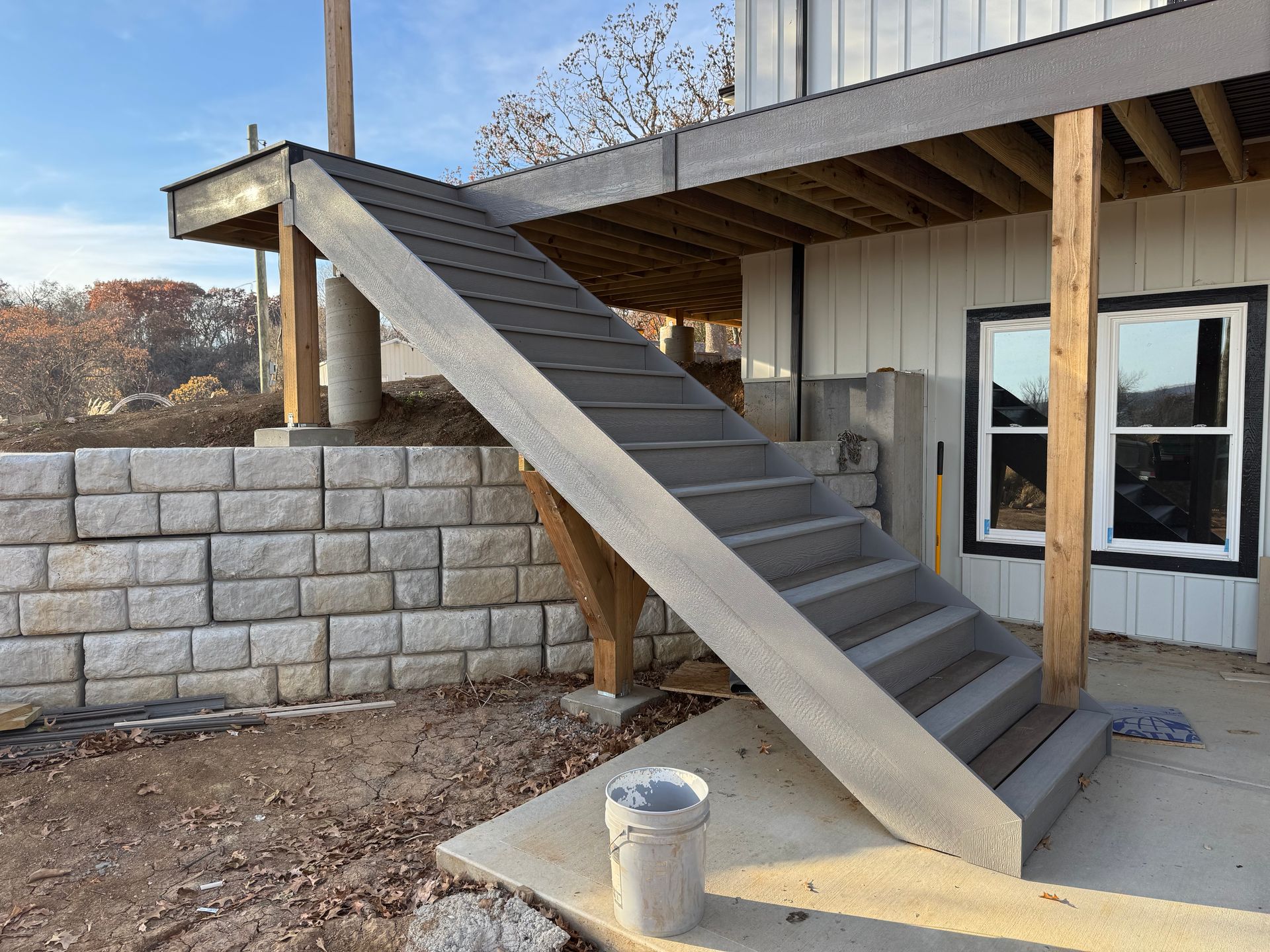Outdoor concrete stairs leading to a raised porch beside a building with a stone retaining wall