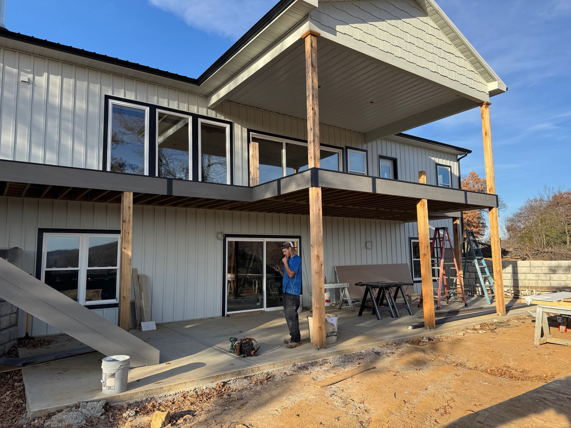Two-story modern house under construction with workers, unfinished siding, and exposed porch posts