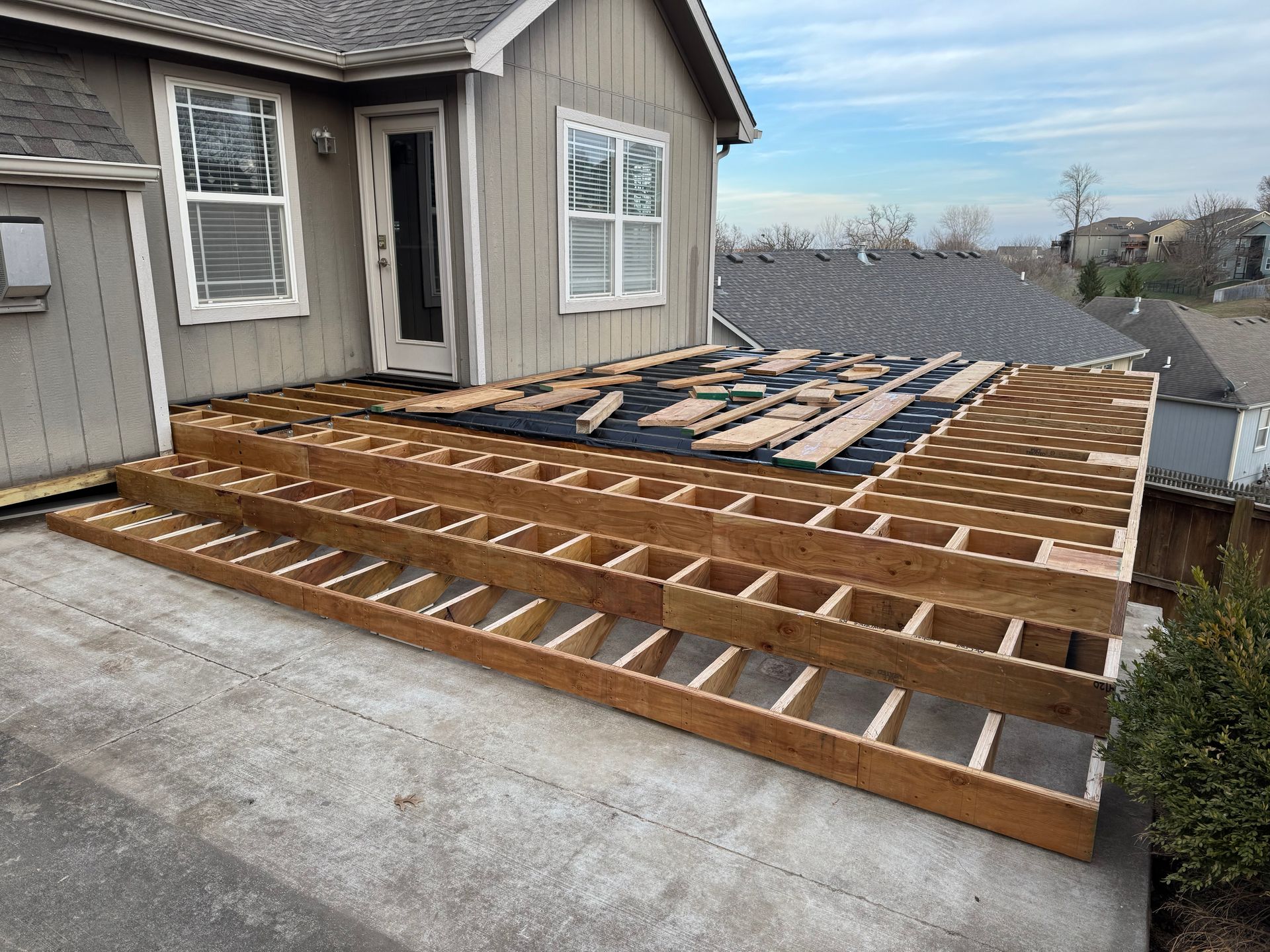 House deck under construction with exposed wooden framing beside gray siding