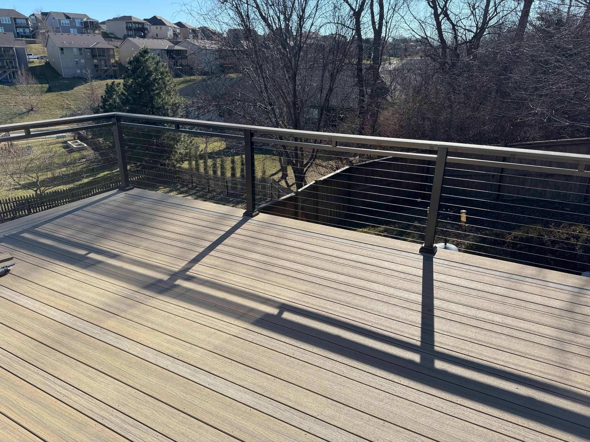 Wooden deck with black railing overlooking a sunny wooded neighborhood