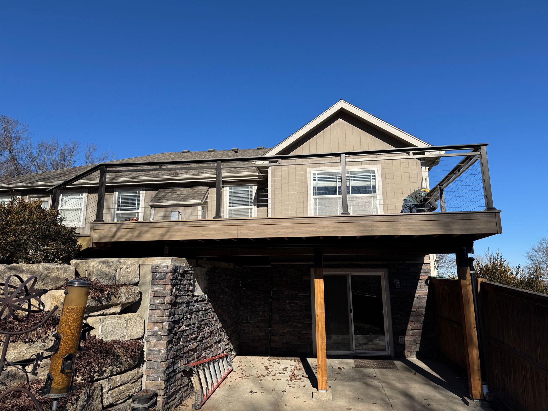 Damaged two-story house with exposed deck and boarded lower level under a clear blue sky